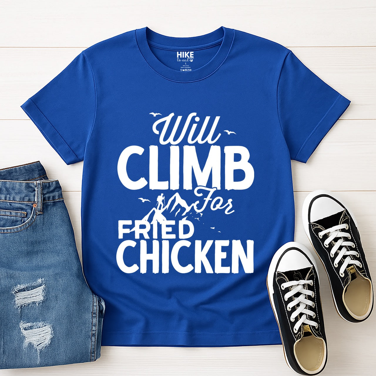 Royal Blue  Will climb for Fried Chicken statement tee with bold and script typography, mountain peaks, climber silhouette, and flying birds for chicken-loving outdoor athletes, climbers, hikers and foodies laid flat with pants and shoes