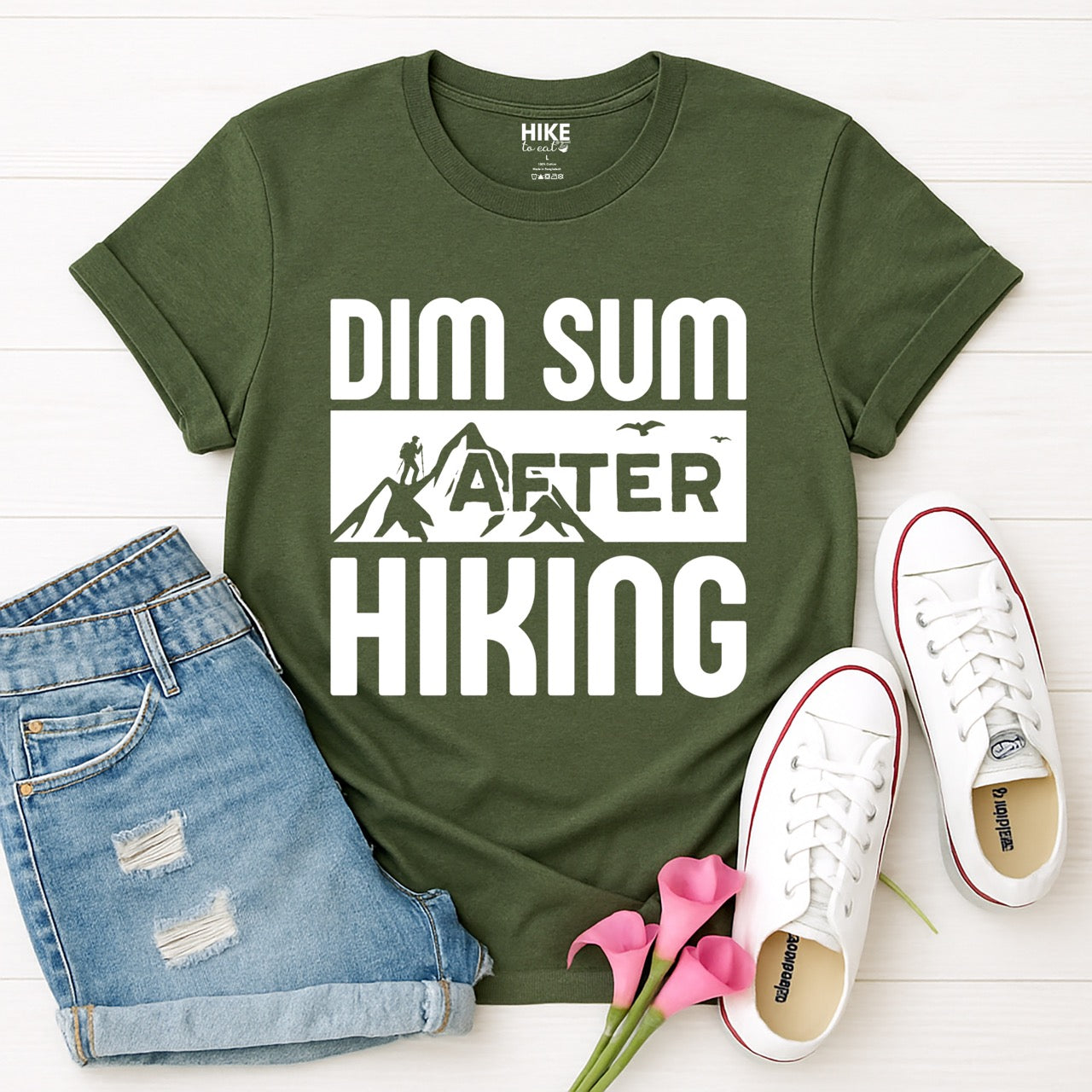 Military Green Dim Sum after Hiking statement tee with bold typography, mountain peaks, hiker silhouette, and flying birds for Chinese food-loving outdoor enthusiasts, hikers and foodies laid flat with shoes and pants
