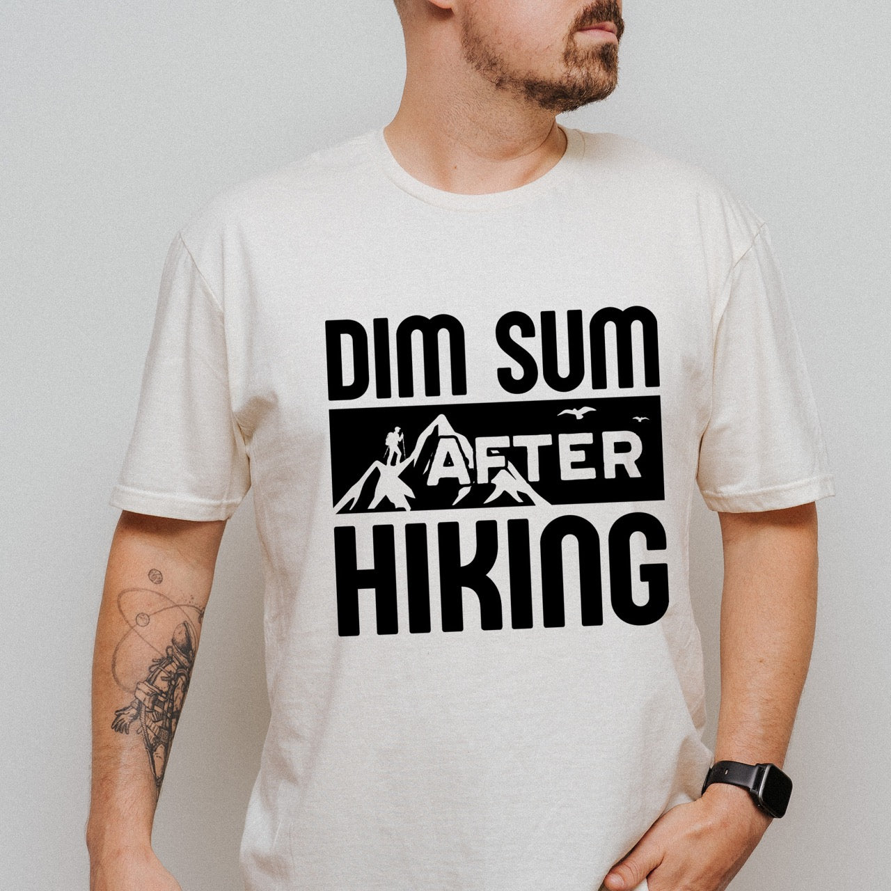 man wearing Natural (beige)  Dim Sum after Hiking statement tee with bold typography, mountain peaks, hiker silhouette, and flying birds for Chinese food-loving outdoor enthusiasts, hikers and foodies
