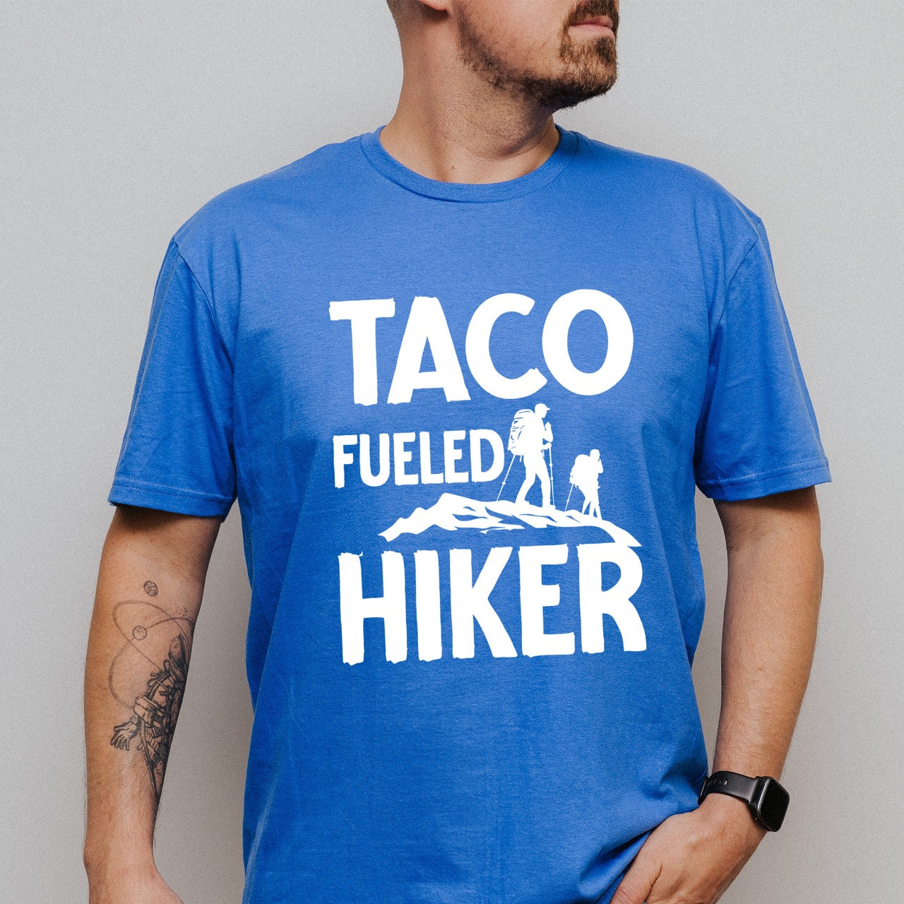 Man wearing Royal blue Taco Fueled Hiker statement tee with bold distressed typography and two hiker silhouettes on mountain ridge for Mexican food-loving outdoor enthusiasts, hikers and foodies