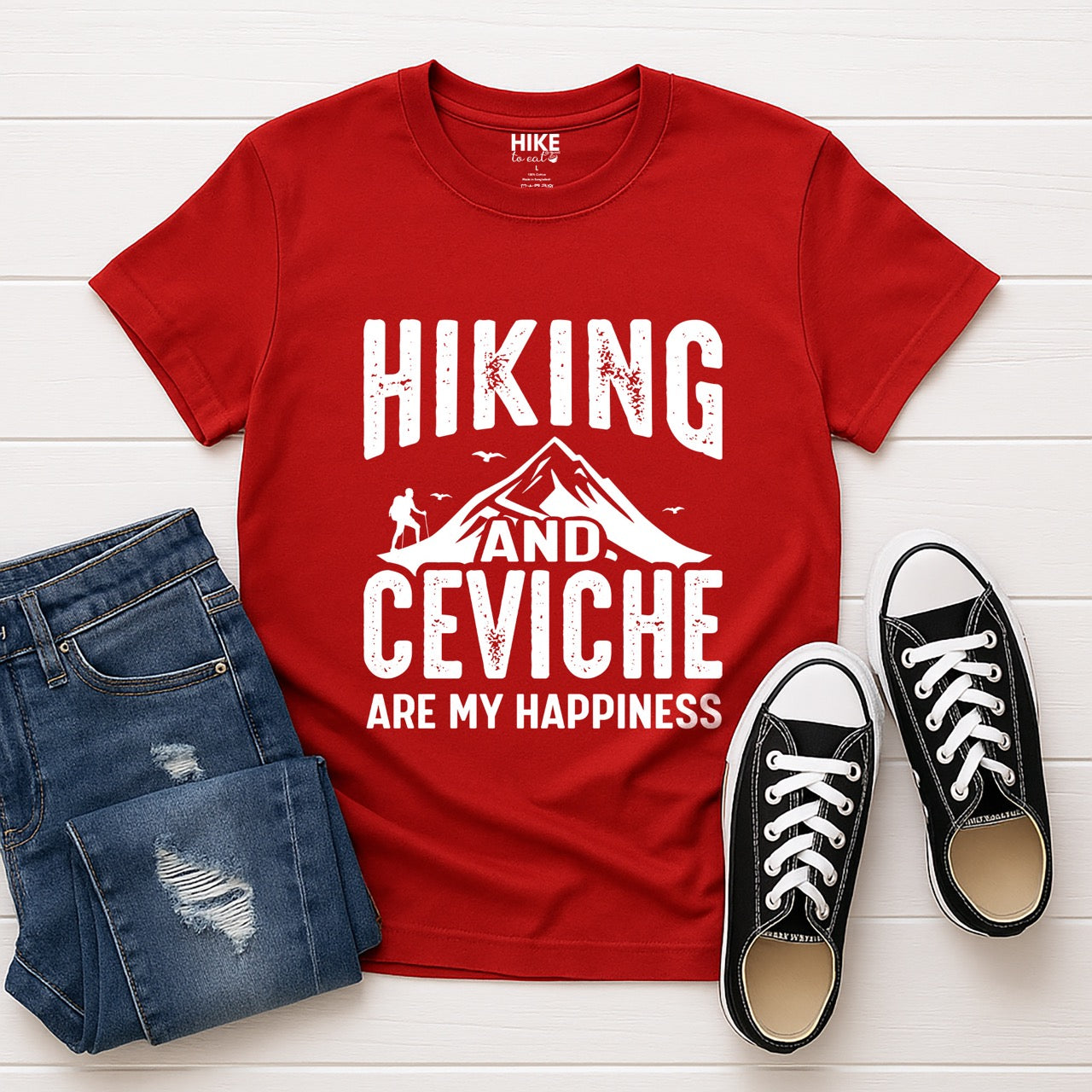 Red Hiking and Ceviche are my Happiness statement tee with distressed bold typography, mountain peaks, hiker silhouette, and flying birds for seafood-loving outdoor enthusiasts, foodies and hikers laid in flat with pants and shoes