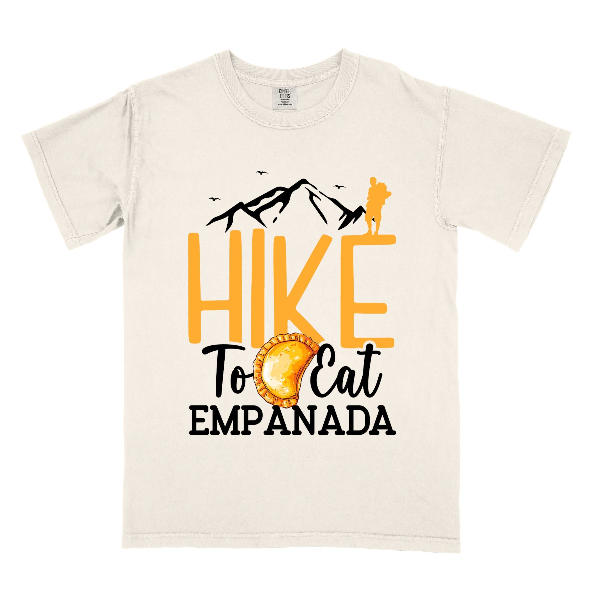 Ivory "Hike to eat empanada" colored vintage tee with bold typography, illustrated freshly baked empanada, mountains, birds, and backpackers for street food enthusiasts.