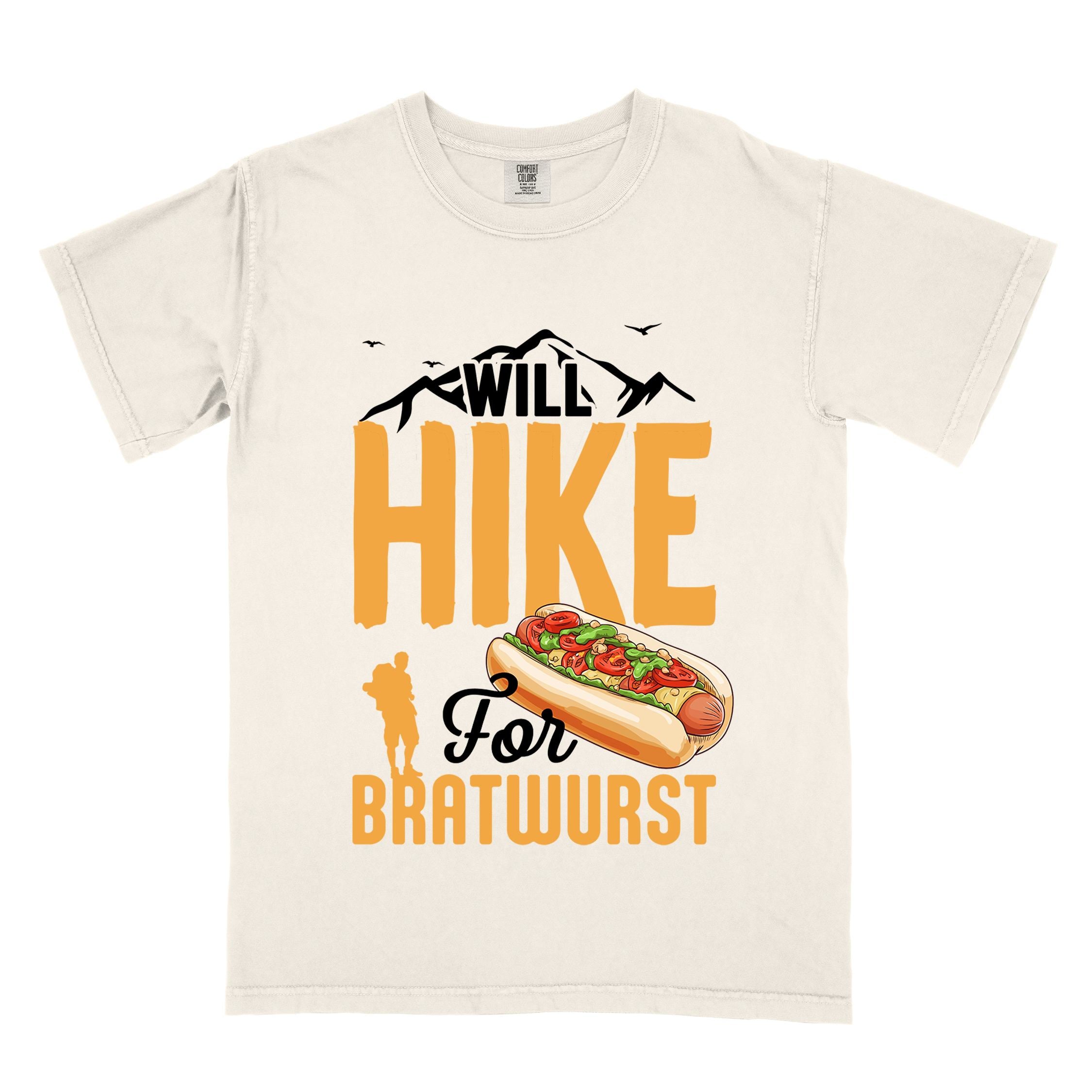 Ivory "Will hike for bratwurst" colored vintage tee with bold typography, illustrated bratwurst in a bun, mountains, birds, and backpackers for street food enthusiasts.