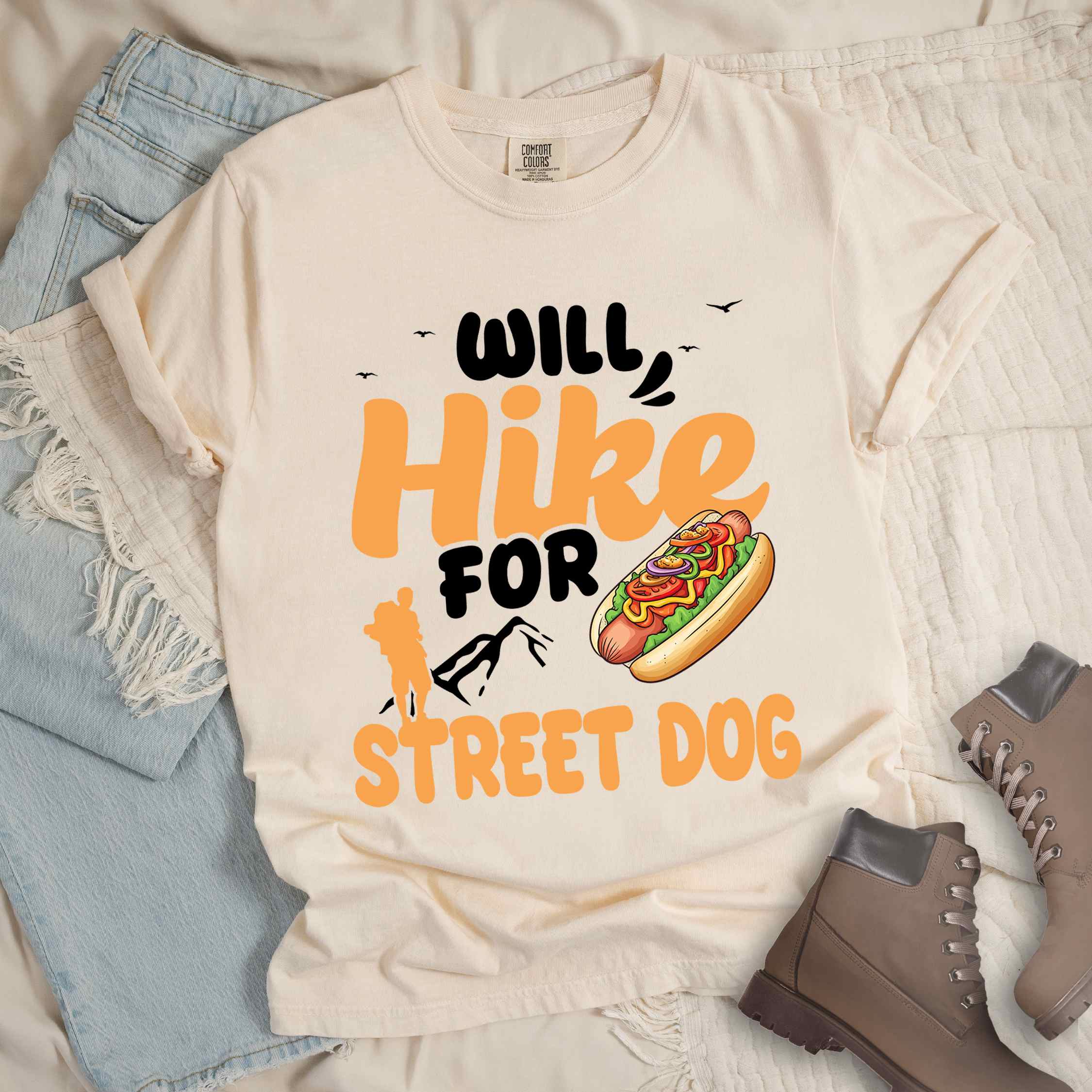 Ivory "Will hike for street dog" colored vintage tee with bold typography, illustrated freshly bratwurst in a bun, mountains, birds, and backpackers for street dog lovers.