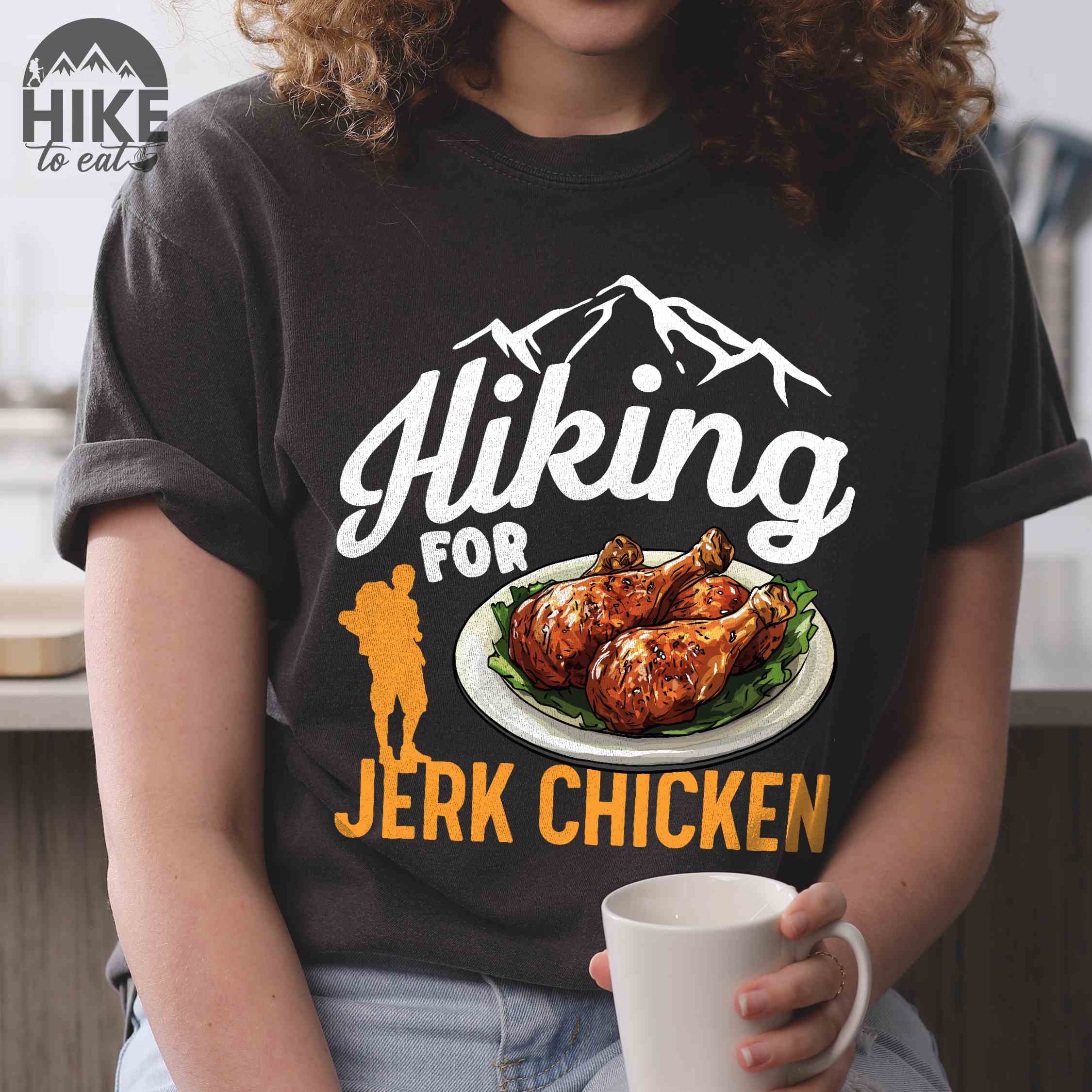 Woman wearing pepper "hiking for jerk chicken" colored vintage tee with bold typography, illustrated jerk chicken on a plate, mountains, birds, and backpackers for bbq chicken lovers.