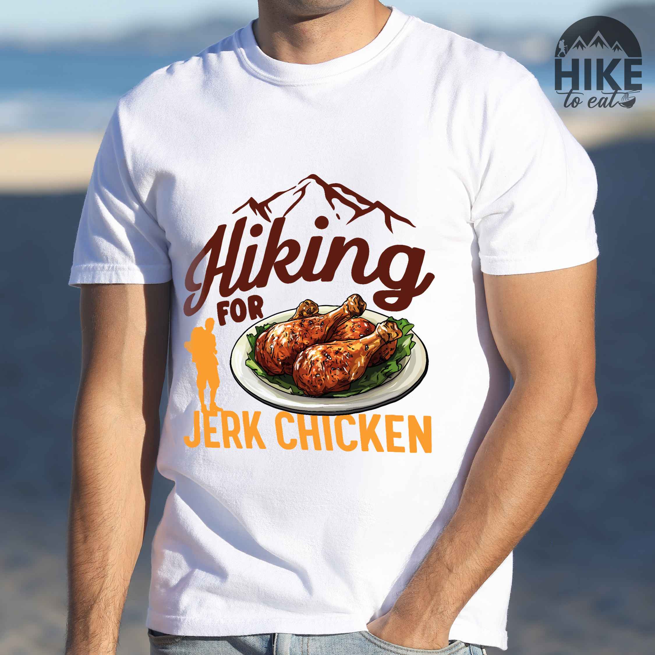 Man wearing white "hiking for jerk chicken" colored vintage tee with bold typography, illustrated jerk chicken on a plate, mountains, birds, and backpackers for bbq chicken lovers.