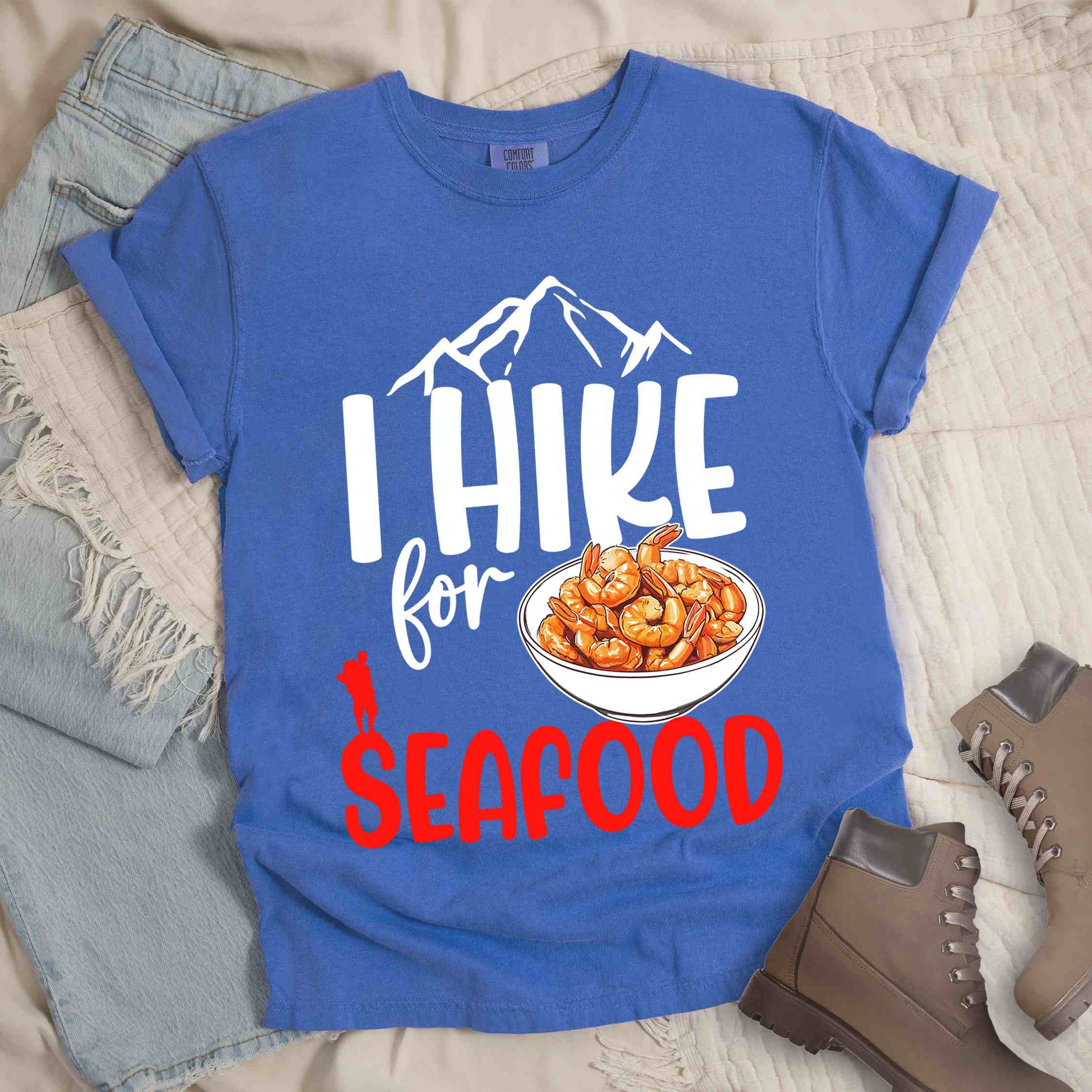 flo blue "I hike for seafood" colored vintage tee with bold typography, illustrated shrimps on a bowl, mountains, birds, and backpackers for seafood  lovers.