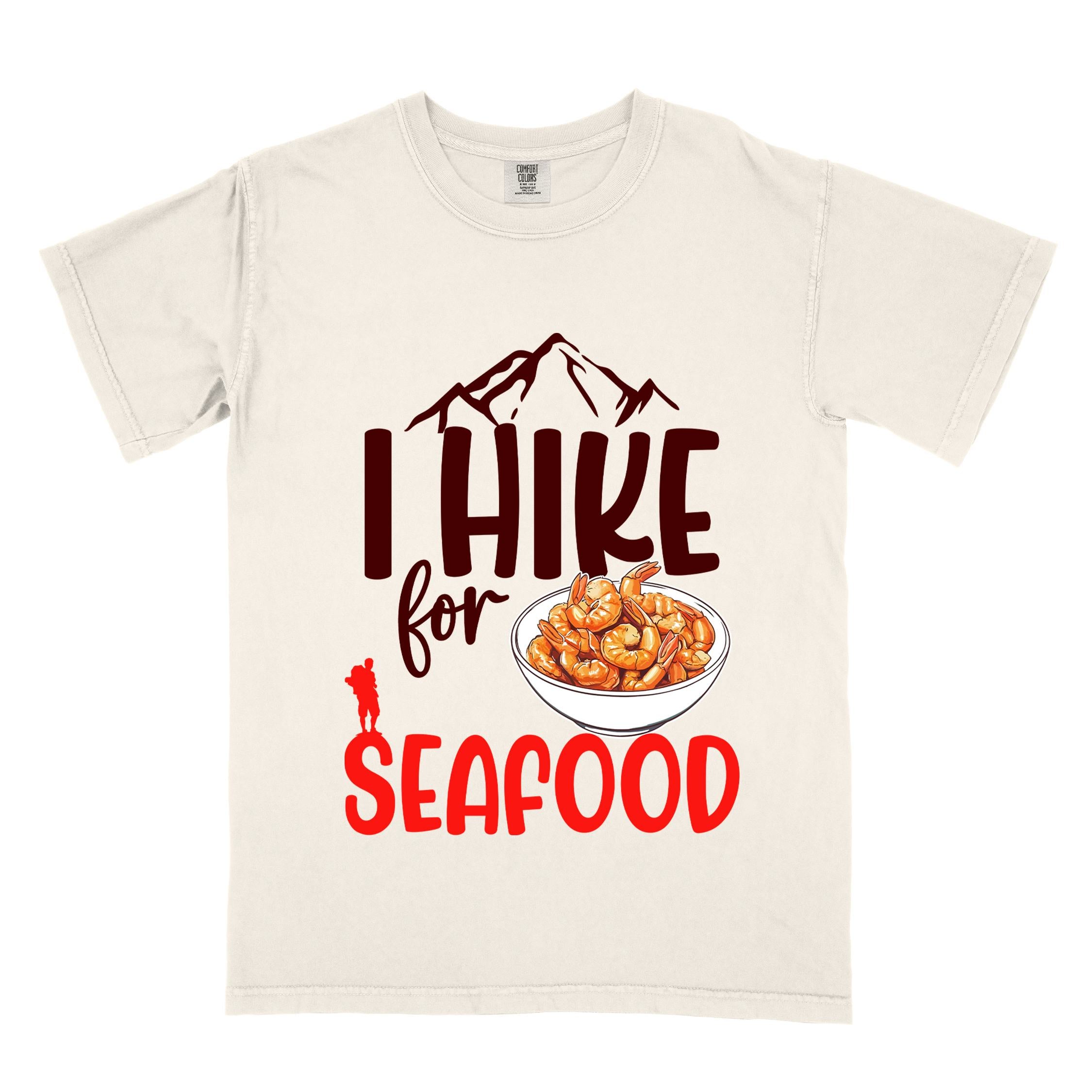 Ivory "I hike for seafood" colored vintage tee with bold typography, illustrated shrimps on a bowl, mountains, birds, and backpackers for seafood  lovers.