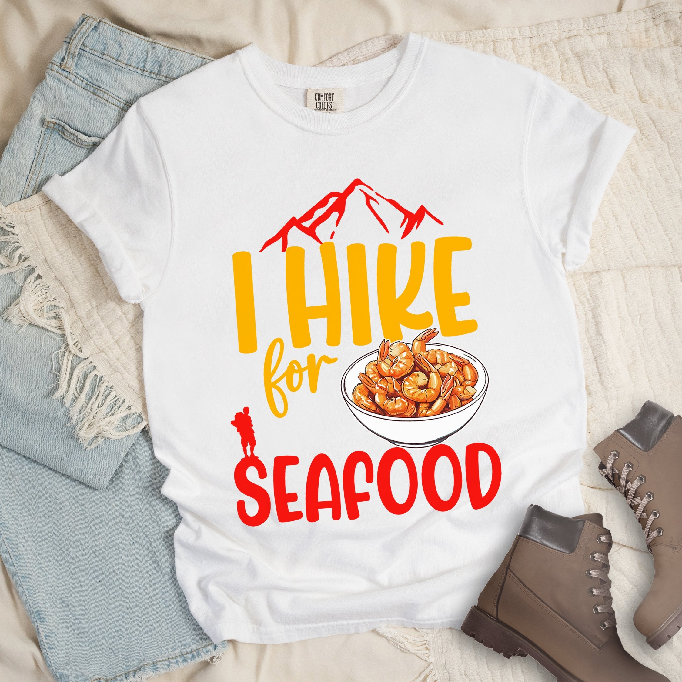 White shirt with Hiking Design featuring the phrase “I Hike for Seafood” and an illustration of a bowl of shrimp with a hiker silhouette.