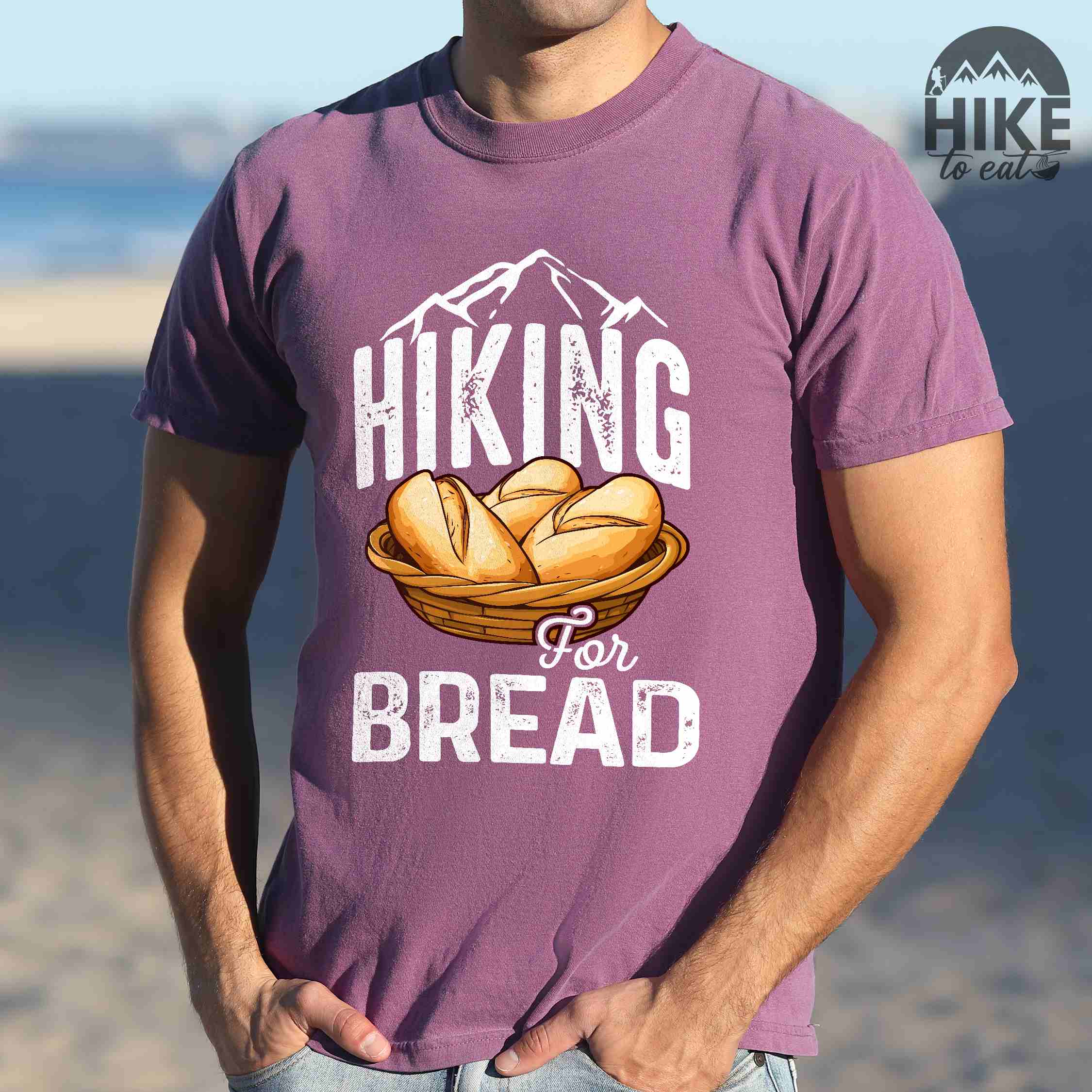 Man wearing berry "Hiking for bread" colored statement tee with flowing script typography, bold lettering, and freshly baked bread illustration for pastry-loving outdoor enthusiasts, hikers and foodies