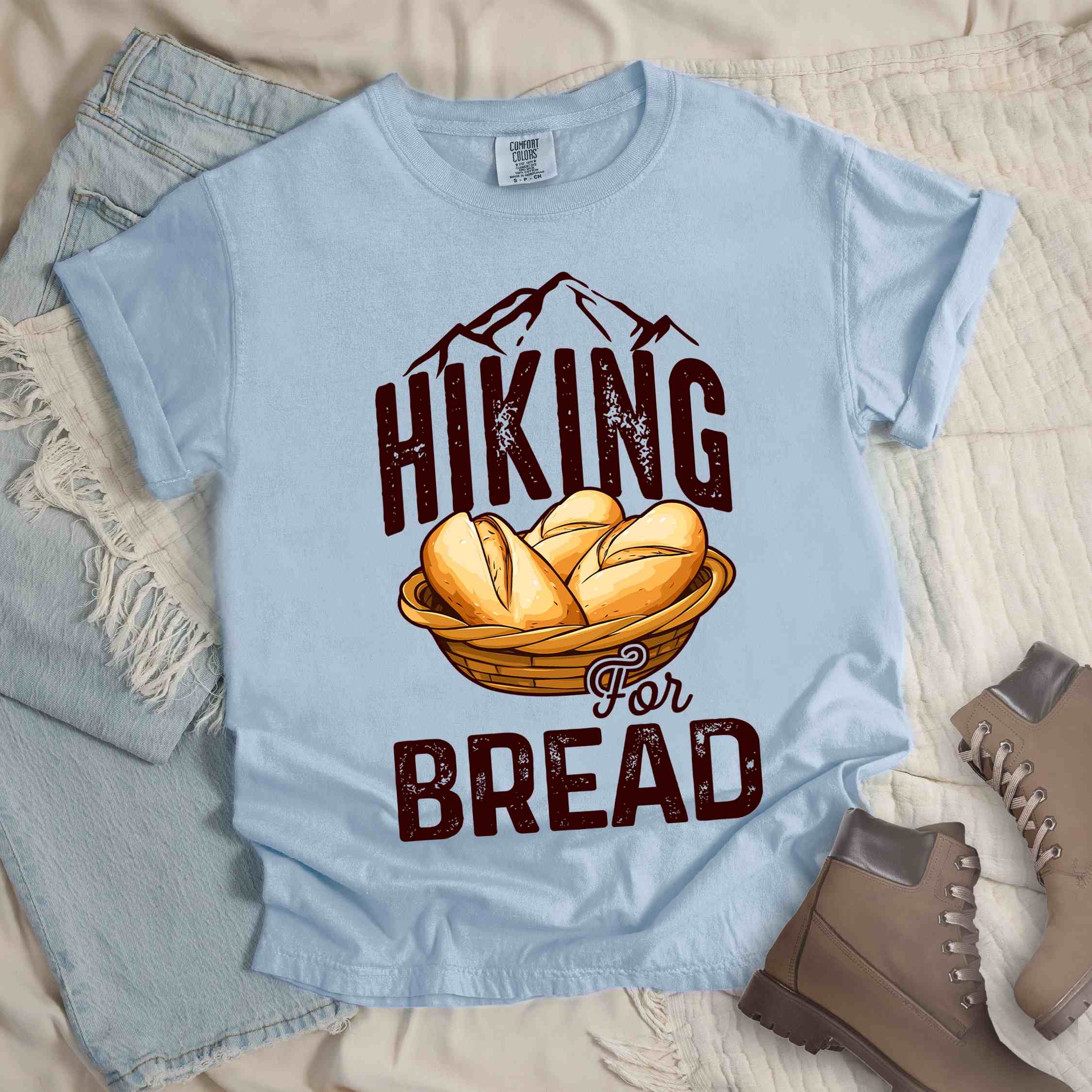 Chambray "Hiking for bread" colored statement tee with flowing script typography, bold lettering, and freshly baked bread illustration for pastry-loving outdoor enthusiasts, hikers and foodies