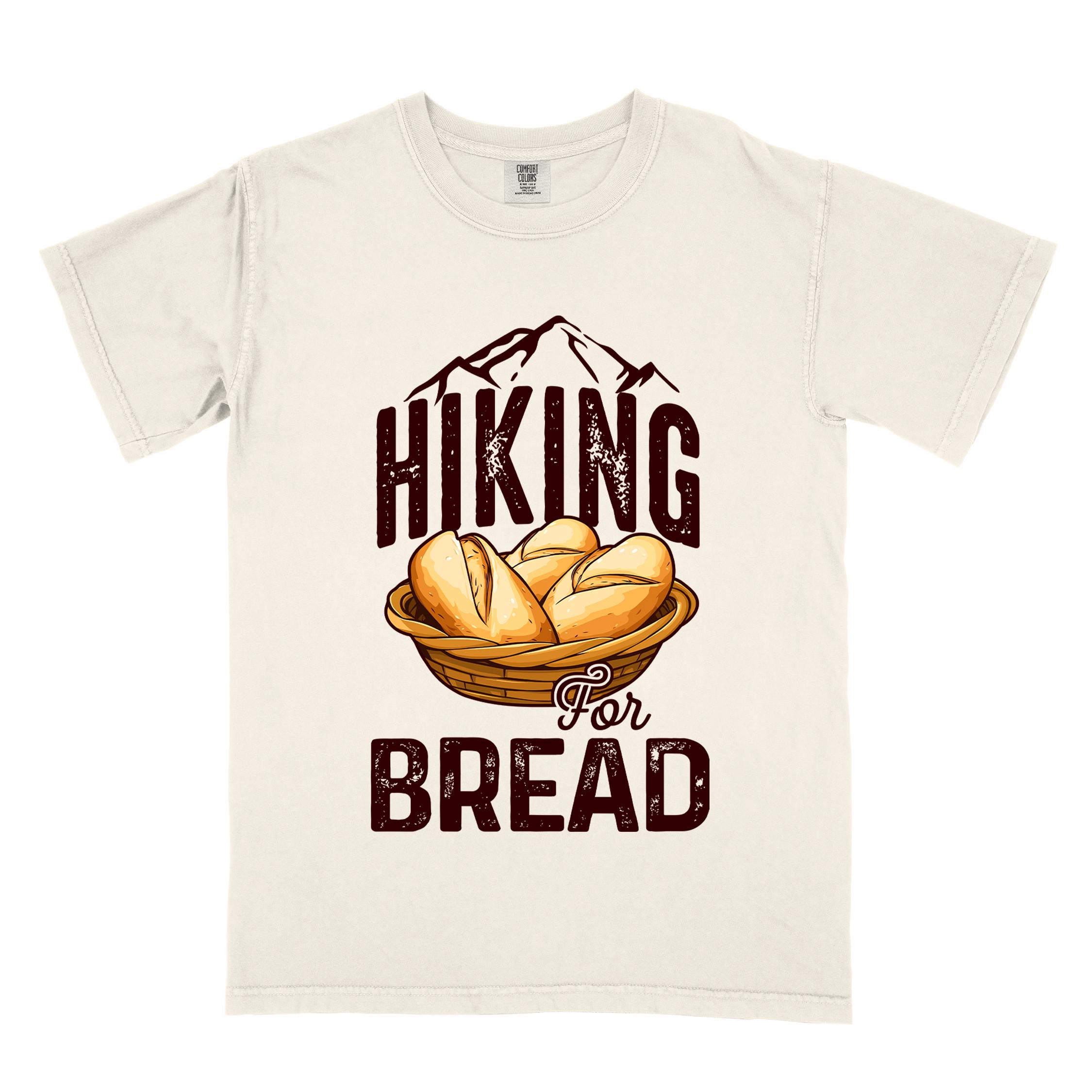 Ivory "Hiking for bread" colored statement tee with flowing script typography, bold lettering, and freshly baked bread illustration for pastry-loving outdoor enthusiasts, hikers and foodies