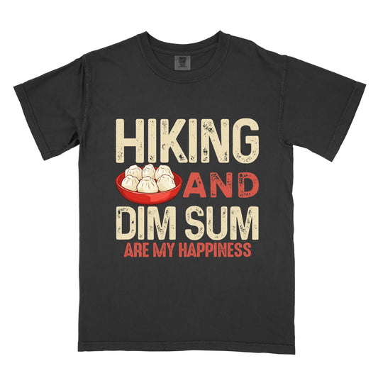 Black t-shirt with beige and red distressed text reading "HIKING AND DIM SUM ARE MY HAPPINESS". "HIKING" appears in large beige distressed letters at the top, "AND" in red distressed text in the middle, "DIM SUM" in large beige distressed letters below it, and "ARE MY HAPPINESS" in smaller red text at the bottom. Features an illustration of six steamed dumplings in a red bowl between "HIKING" and "AND".