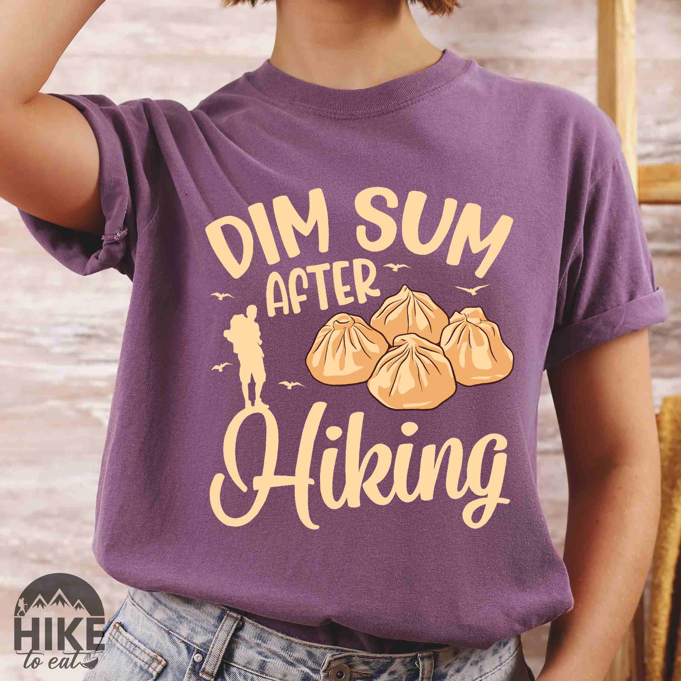 Woman wearing berry "dim sum after hiking" colored statement tee with bold typography, and steamed dim sum illustration for dim sum-loving outdoor enthusiasts, hikers and foodies