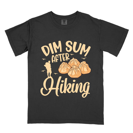 Black t-shirt with beige text reading "DIM SUM AFTER Hiking". "DIM SUM" appears in large beige letters at the top, "AFTER" in smaller beige text in the middle, and "Hiking" in beige script at the bottom. Features an illustration of four steamed dumplings in the center, small beige flying birds, and a beige silhouette of a hiker to the left of "AFTER".