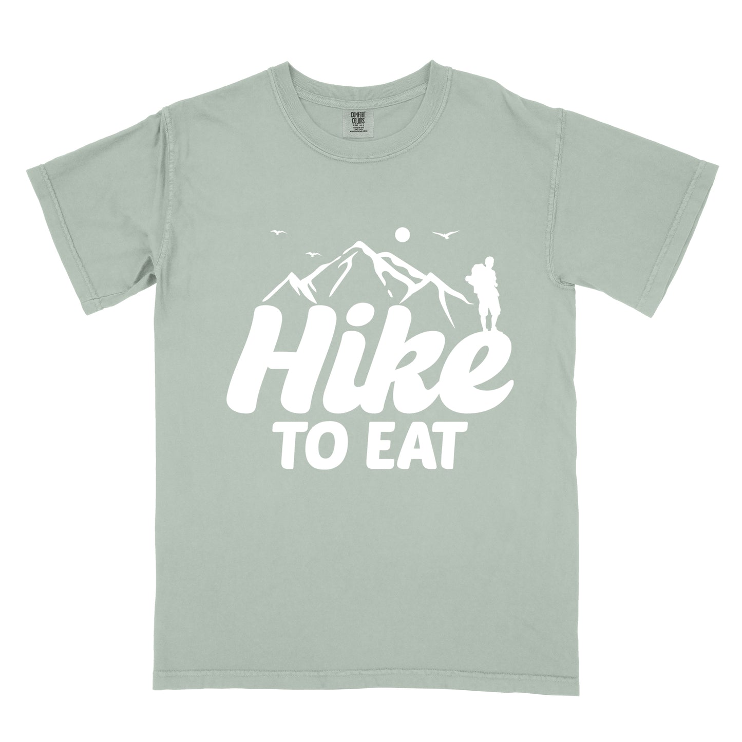 Bay (Light Gray) t-shirt with white text reading "Hike TO EAT". "Hike" appears in large white script letters with white mountain outlines above it, and "TO EAT" in bold white text below it. Features a white silhouette of a hiker to the right of the mountains, white flying birds, and a white circle representing the sun. 
