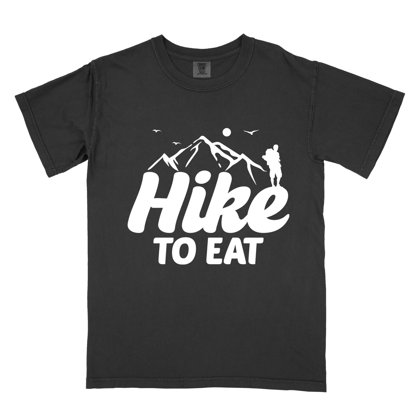 Black t-shirt with white text reading "Hike TO EAT". "Hike" appears in large white script letters with white mountain outlines above it, and "TO EAT" in bold white text below it. Features a white silhouette of a hiker to the right of the mountains, white flying birds, and a white circle representing the sun. 