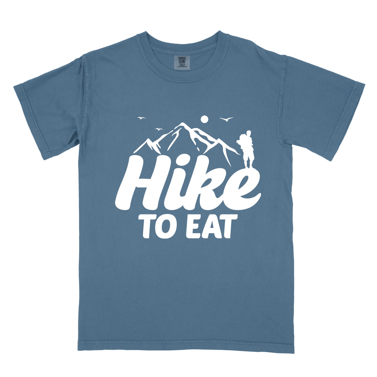 Blue Jean (Denim Blue) t-shirt with white text reading "Hike TO EAT". "Hike" appears in large white script letters with white mountain outlines above it, and "TO EAT" in bold white text below it. Features a white silhouette of a hiker to the right of the mountains, white flying birds, and a white circle representing the sun. 