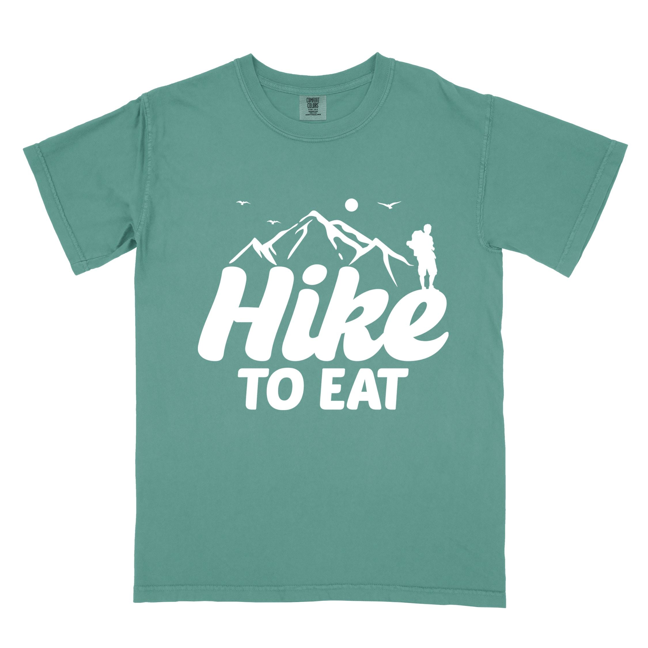 light green "Hike to Eat" colored statement tee with bold typography, mountains, birds, sunrise, perfect for food motivated individuals.