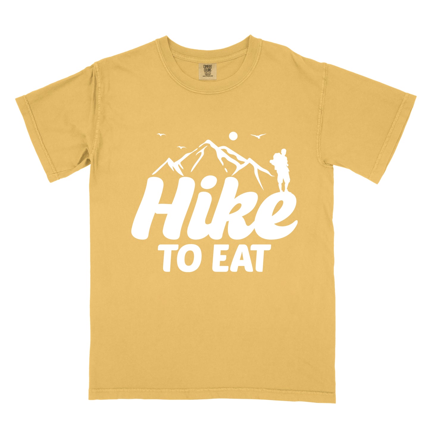 Mustard (Yellow) t-shirt with white text reading "Hike TO EAT". "Hike" appears in large white script letters with white mountain outlines above it, and "TO EAT" in bold white text below it. Features a white silhouette of a hiker to the right of the mountains, white flying birds, and a white circle representing the sun. 