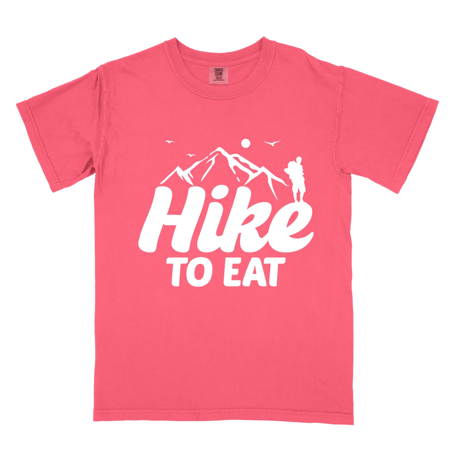 Watermelon (Light Coral) t-shirt with white text reading "Hike TO EAT". "Hike" appears in large white script letters with white mountain outlines above it, and "TO EAT" in bold white text below it. Features a white silhouette of a hiker to the right of the mountains, white flying birds, and a white circle representing the sun. 