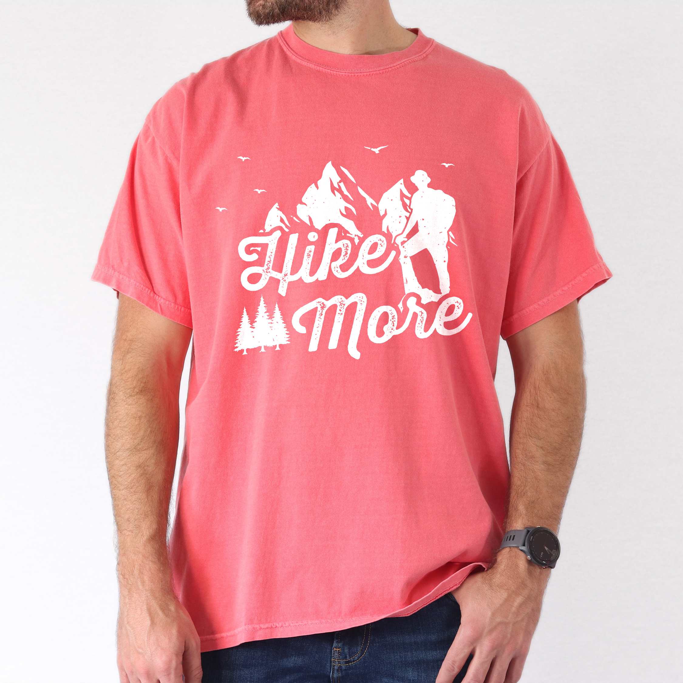 Man wearing watermelon "Hike More" colored statement tee with bold typography, mountains, birds, perfect for food motivated individuals.