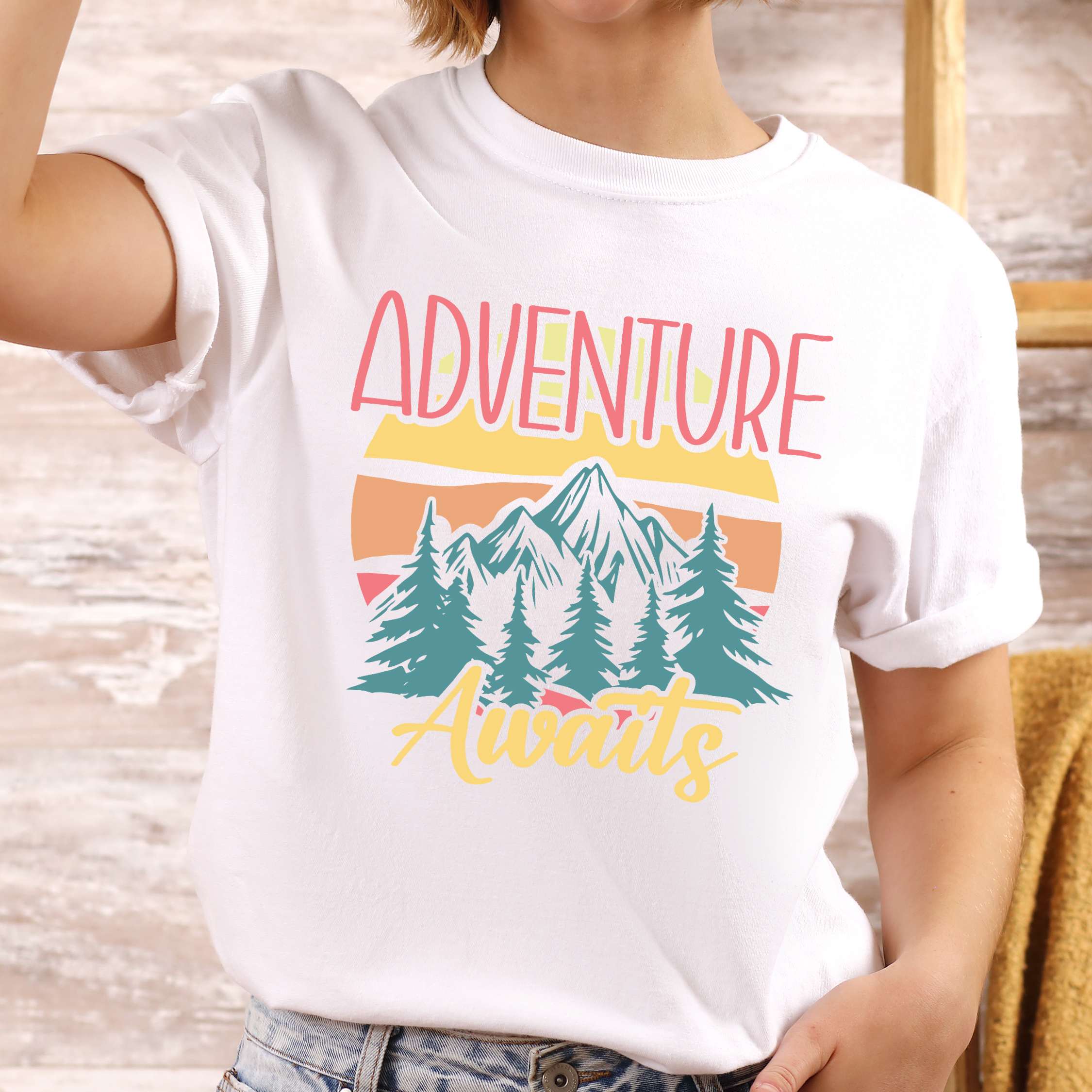 Woman wearing white "Adventure Awaits" colored statement tee with bold typography, mountains, birds, perfect for adventure motivated individuals.