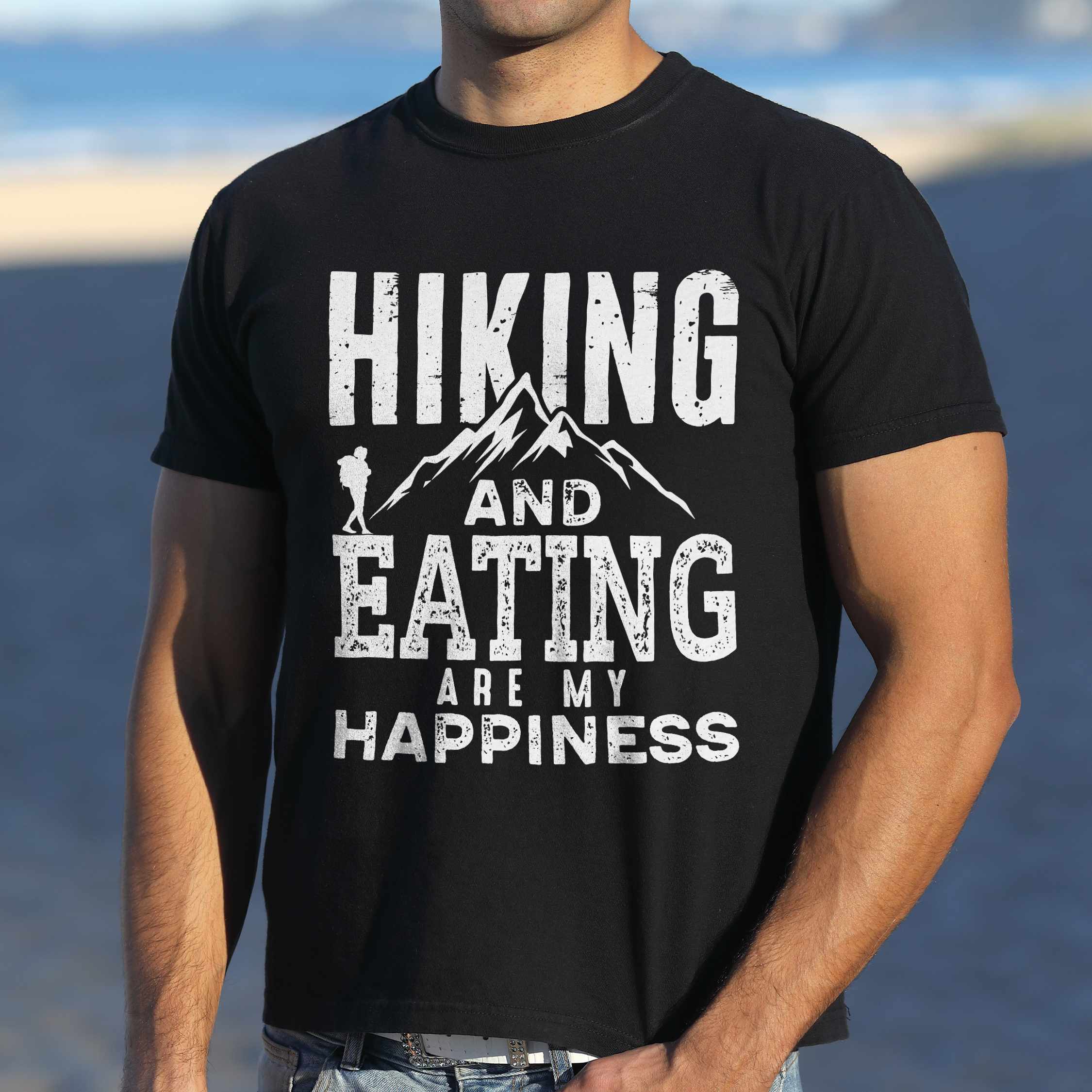 Man wearing black "Hiking and Eating are my happiness" colored statement tee with bold typography, mountains, birds, perfect for adventure motivated individuals.