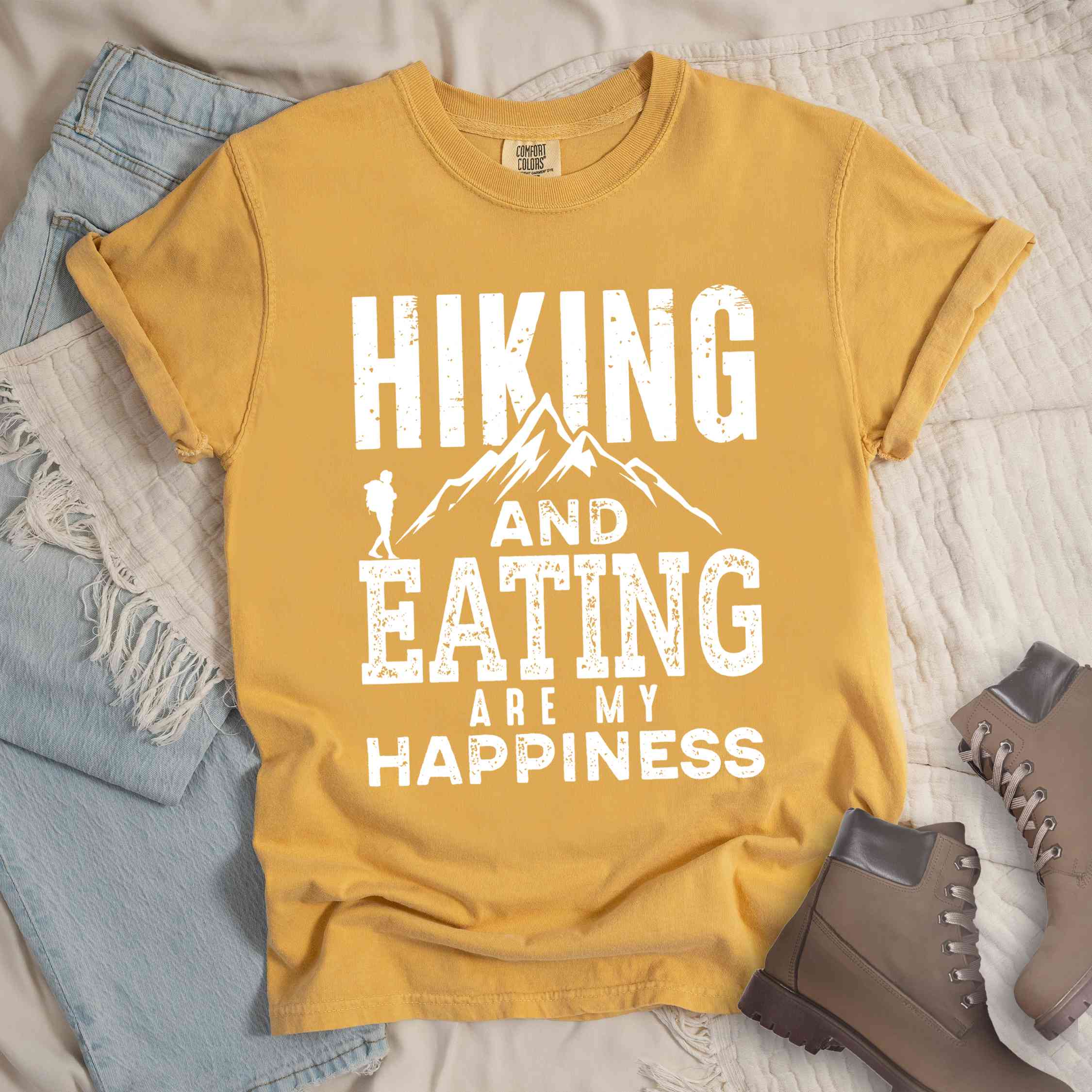 Mustard "Hiking and Eating are my happiness" colored statement tee with bold typography, mountains, birds, perfect for adventure motivated individuals.