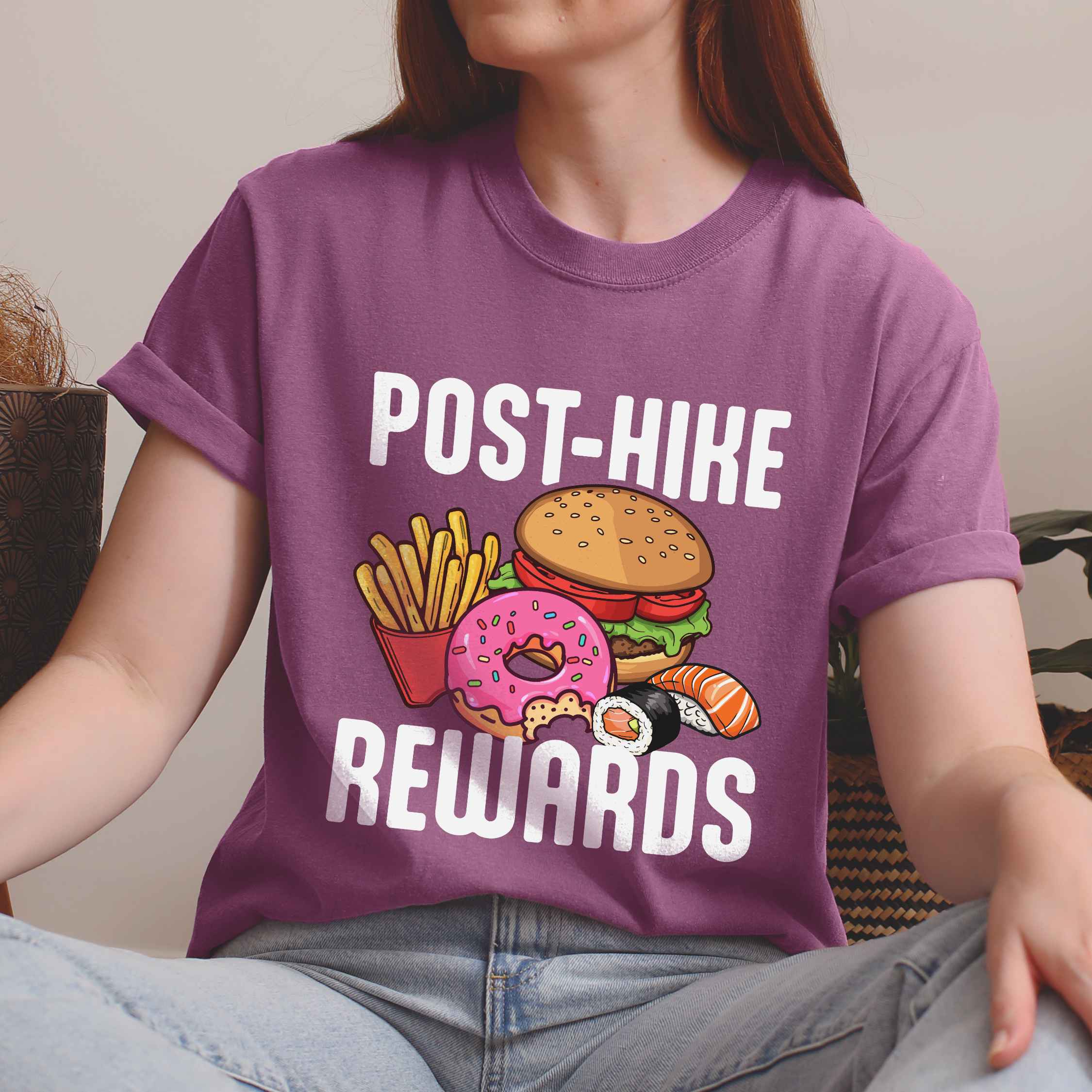 Woman wearing berry "Post-hike rewards" colored statement tee with bold typography, mountains, birds, illustrated fast food meal, perfect for adventure motivated individuals and looking for post-hike meal.