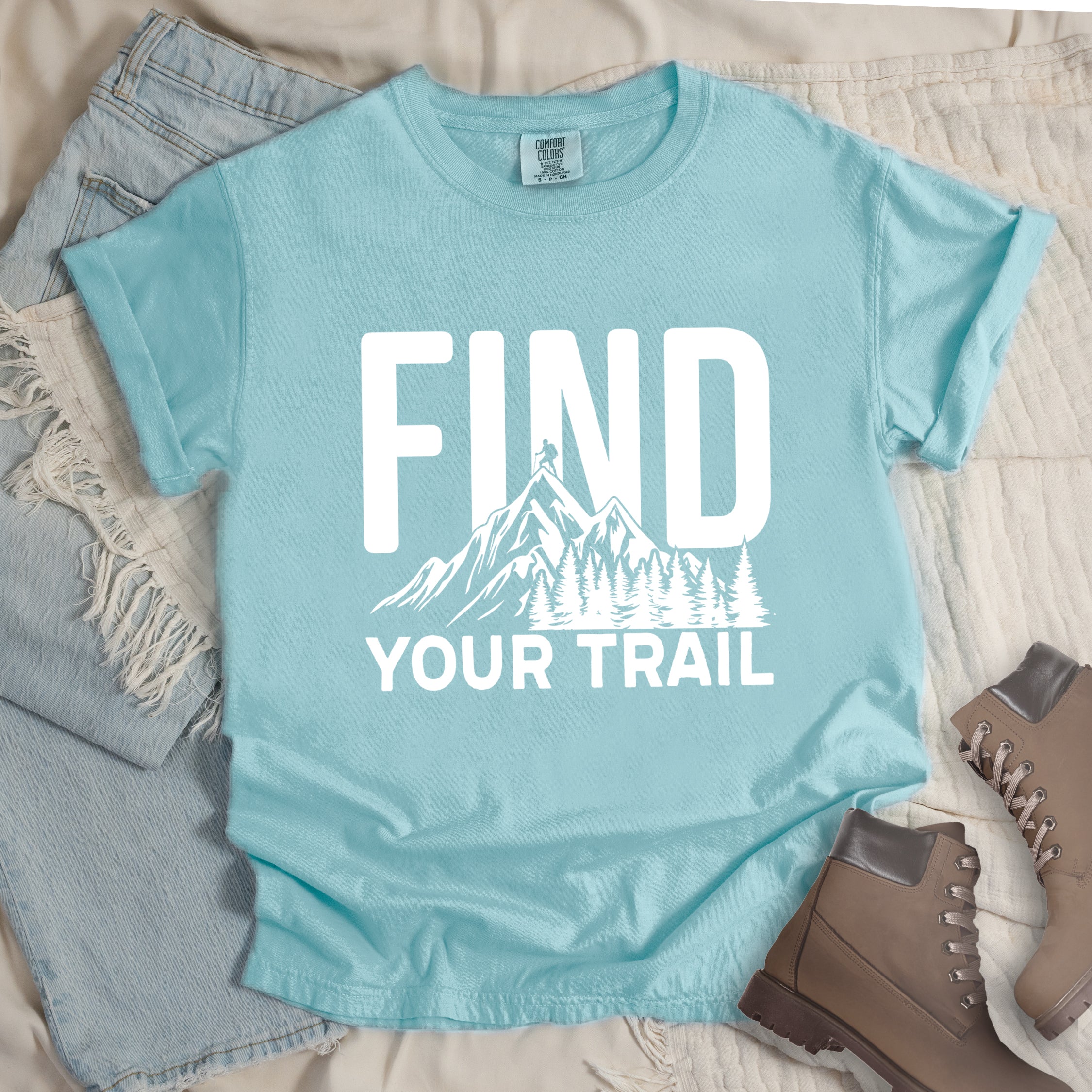 Chalky Mint (Pastel Blue) graphic t-shirt with 'Find Your Trail' text and white mountain and forest design, styled with light wash jeans and brown hiking boots