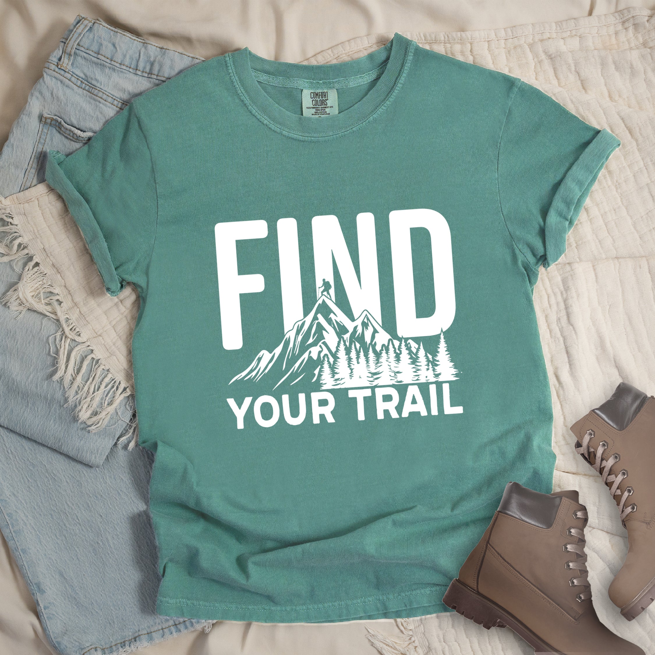 Light Green graphic t-shirt with 'Find Your Trail' text and white mountain and forest design, styled with light wash jeans and brown hiking boots