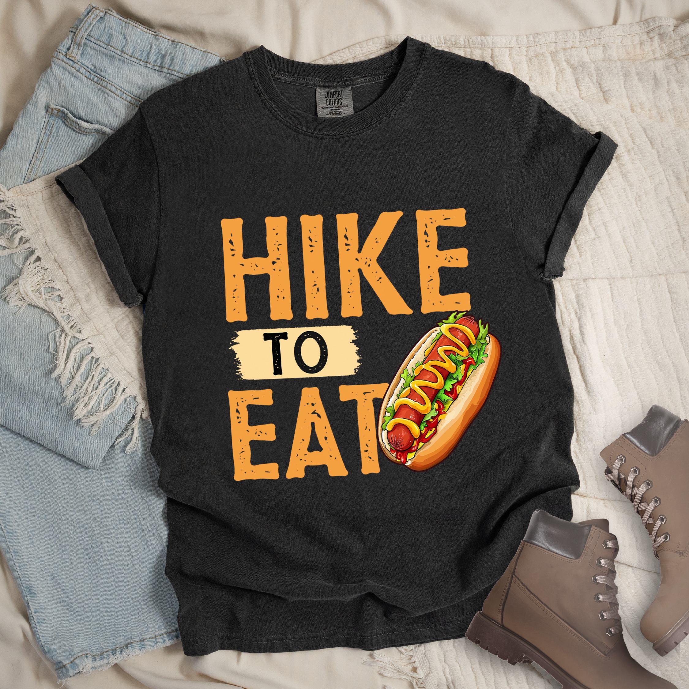 Dark grey shirt showing a hiking design with 'HIKE TO EAT phrase and an illustration of a hotdog in a bun with mustard on top