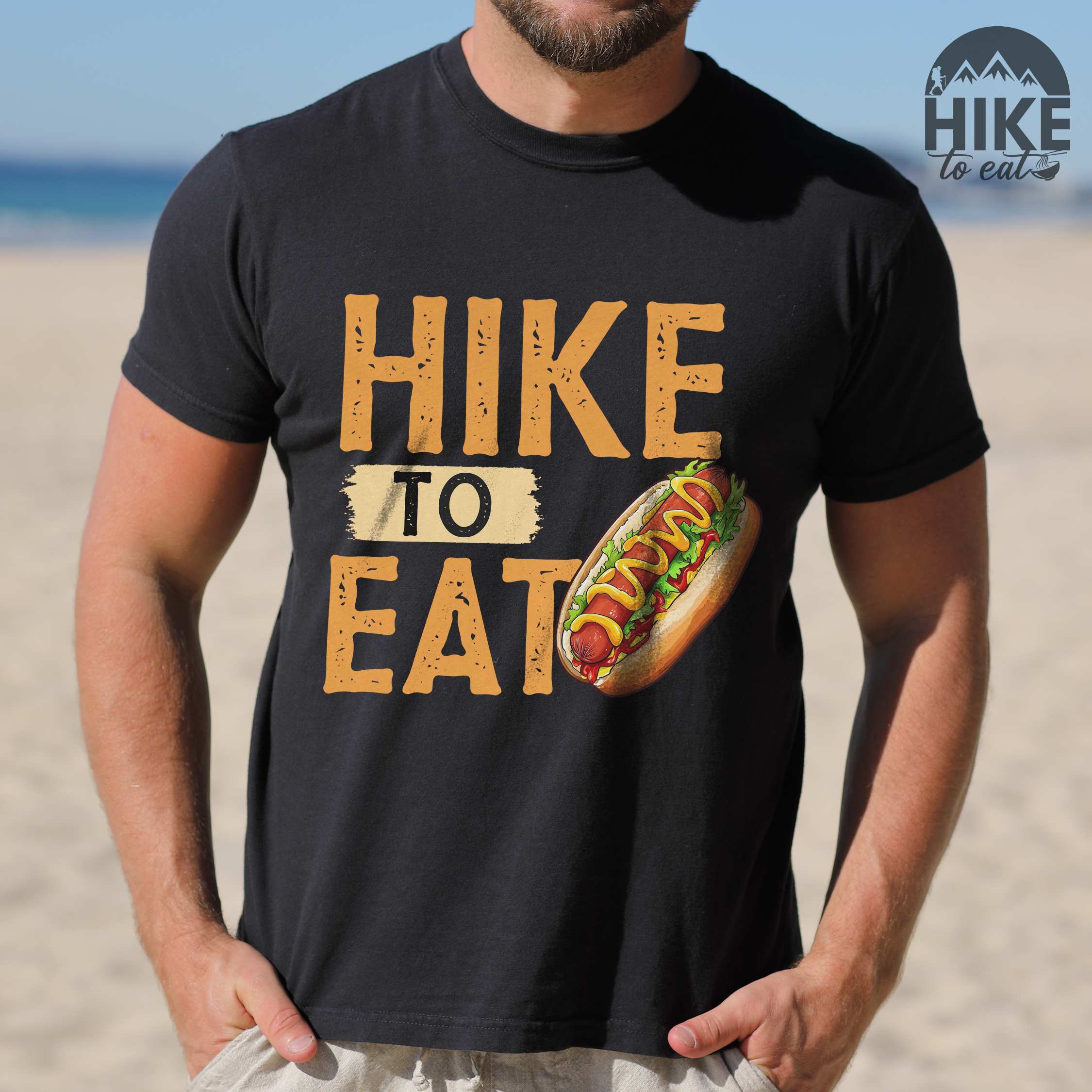 Man wearing black "Hike to Eat" colored vintage tee with bold typography, and illustrated hotdog with mustard and ketchup sauce.