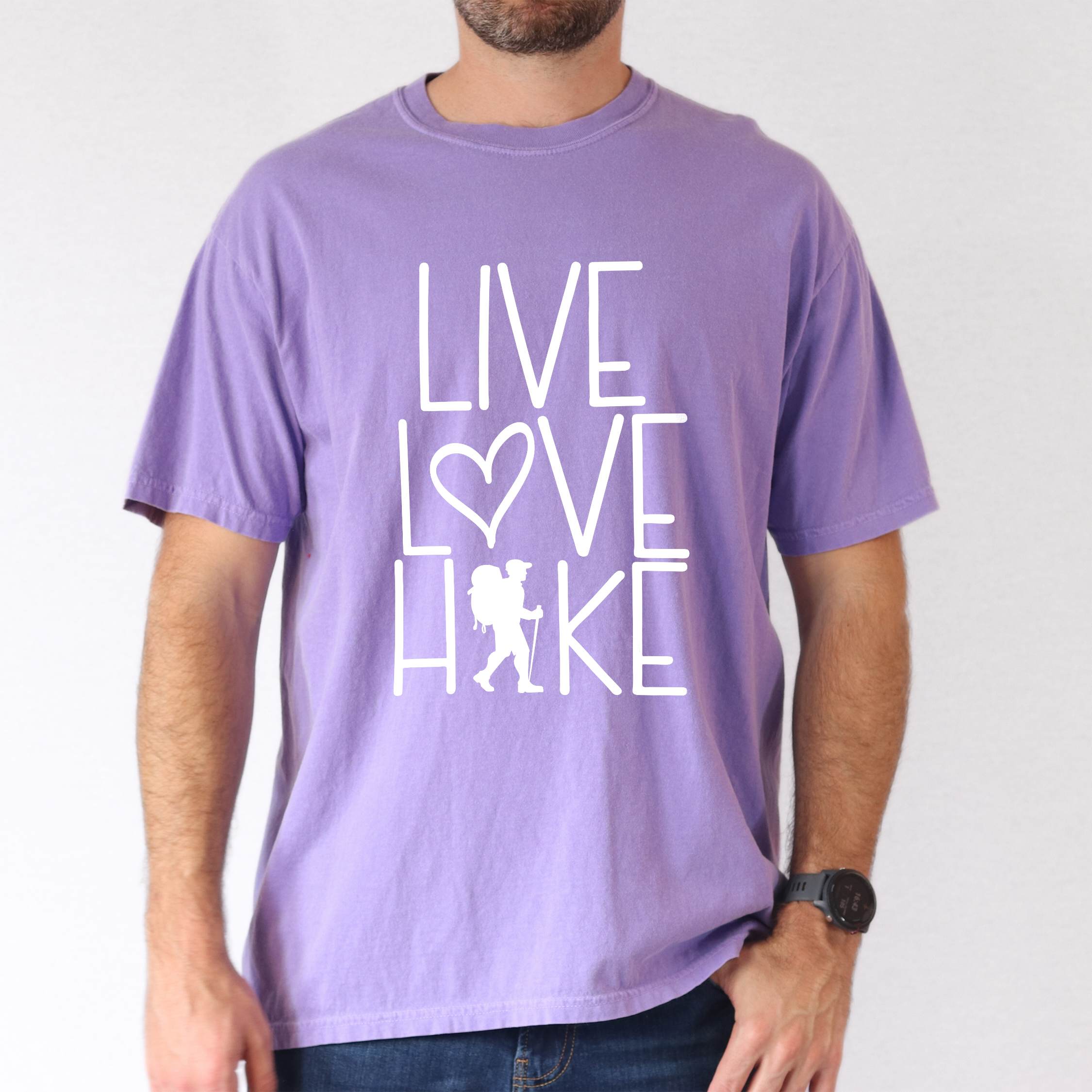 Man wearing violet "Live Love hike" colored statement tee with bold typography, perfect for adventure motivated individuals.