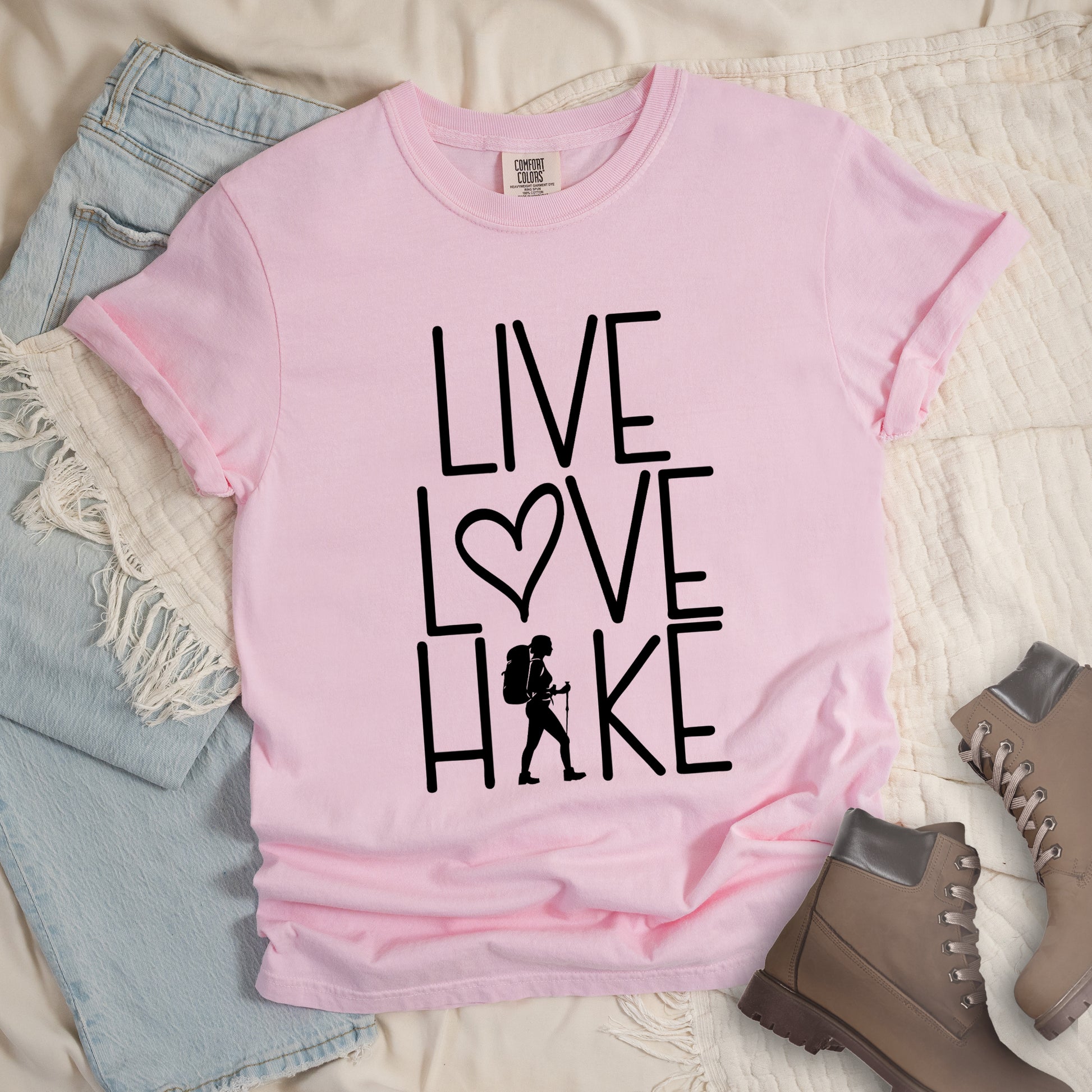 Blossom (Light Pink) t-shirt with black text reading 'Live Love Hike' featuring a heart symbol and female hiker silhouette with backpack and hiking stick. 