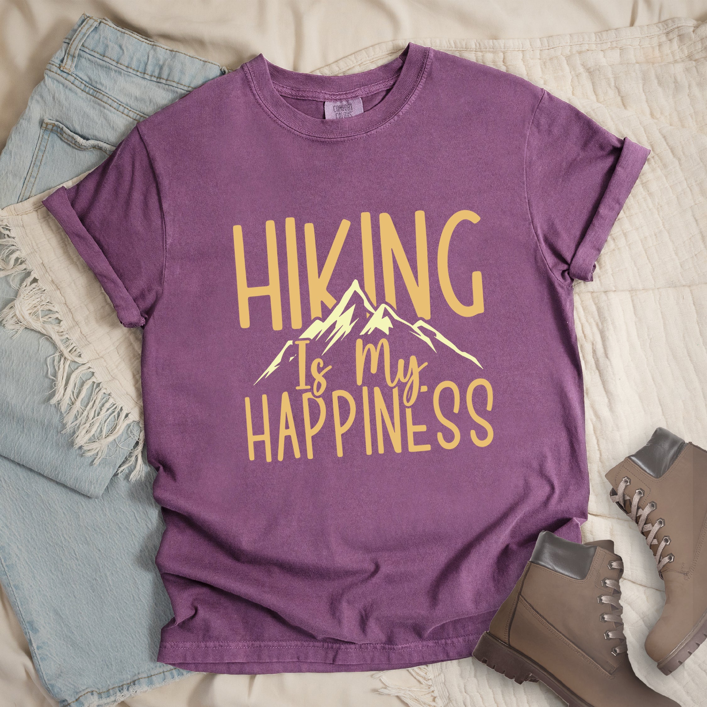 Berry (Dark Violet) graphic t-shirt with 'Hiking Is My Happiness' text in yellow and cream mountain design, styled with light wash jeans and brown hiking boots