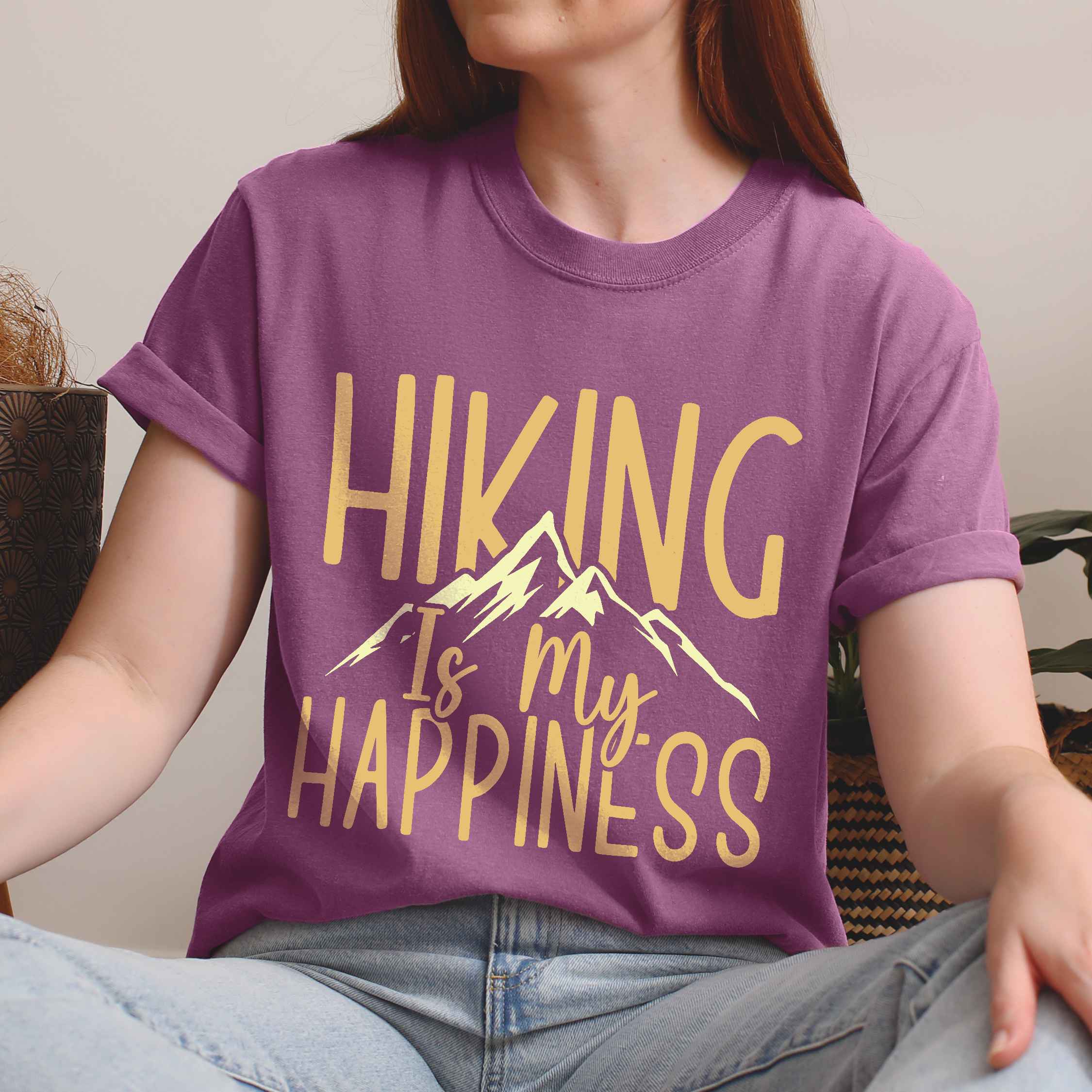 Woman wearing berry "hiking is my happiness" colored statement tee with bold typography, mountain, sunrise, perfect for adventure motivated individuals.