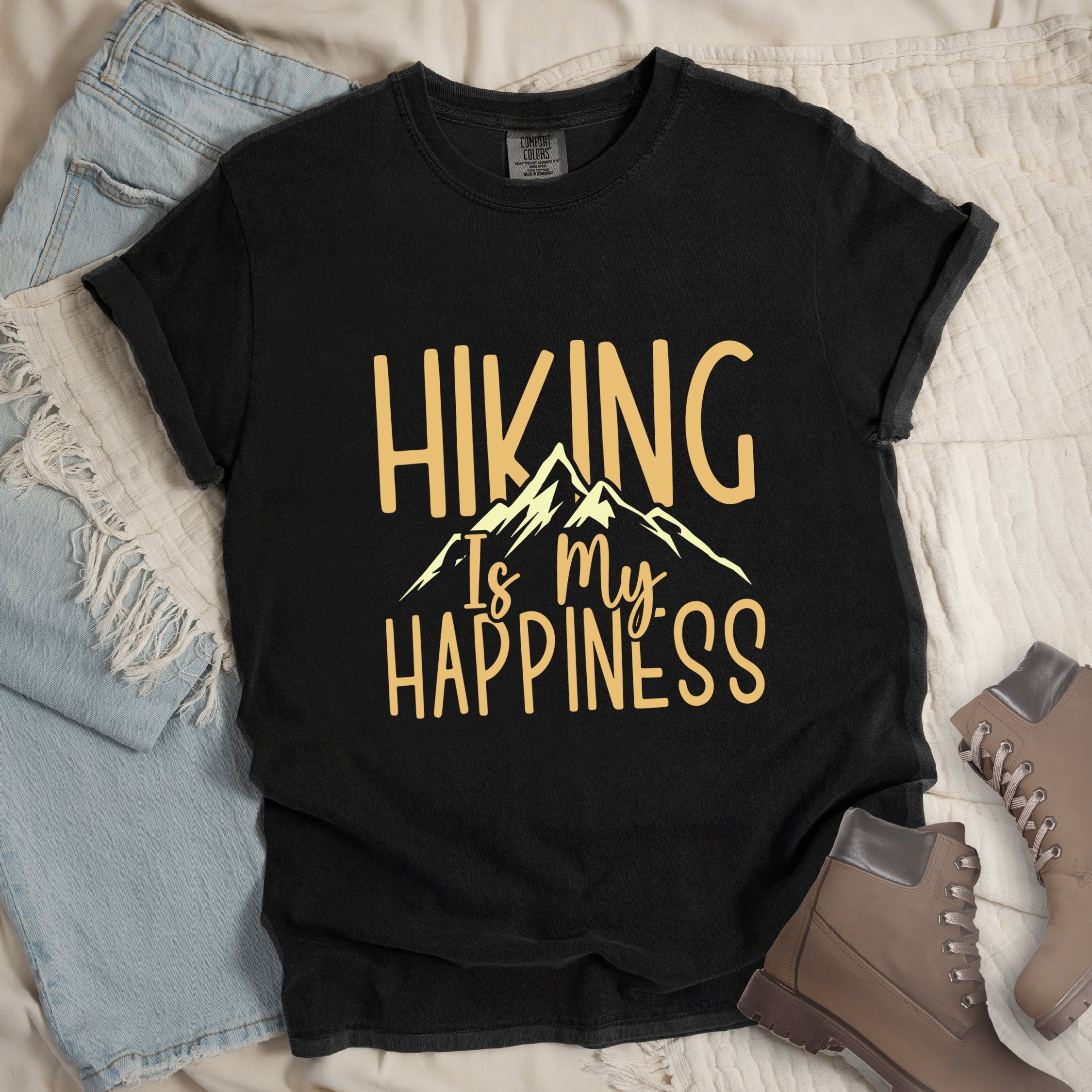 Black graphic t-shirt with 'Hiking Is My Happiness' text in yellow and cream mountain design, styled with light wash jeans and brown hiking boots