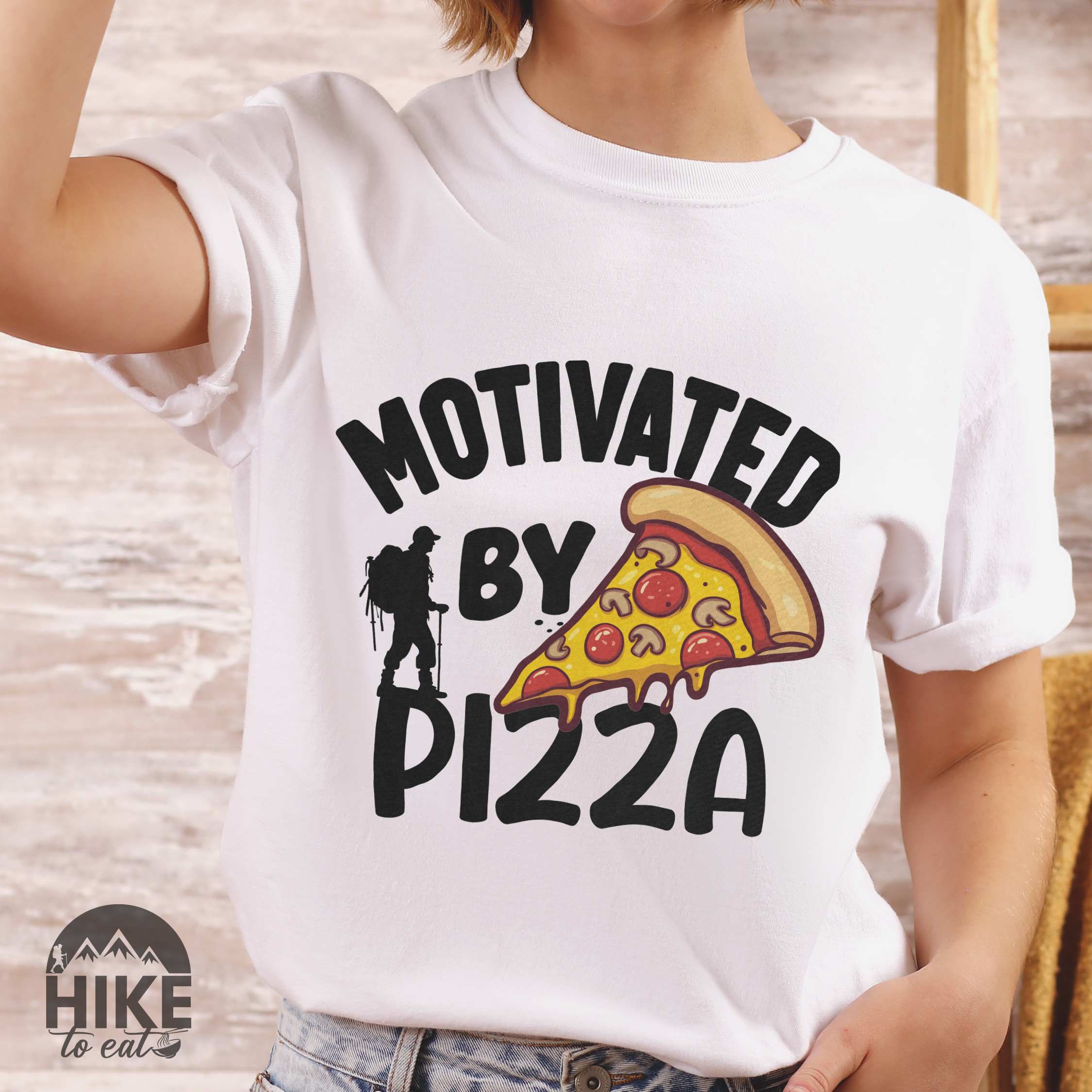 Woman wearing white Motivated by Pizza colored vintage tee with bold typography, illustrated pizza slice, and backpacker for foodies.