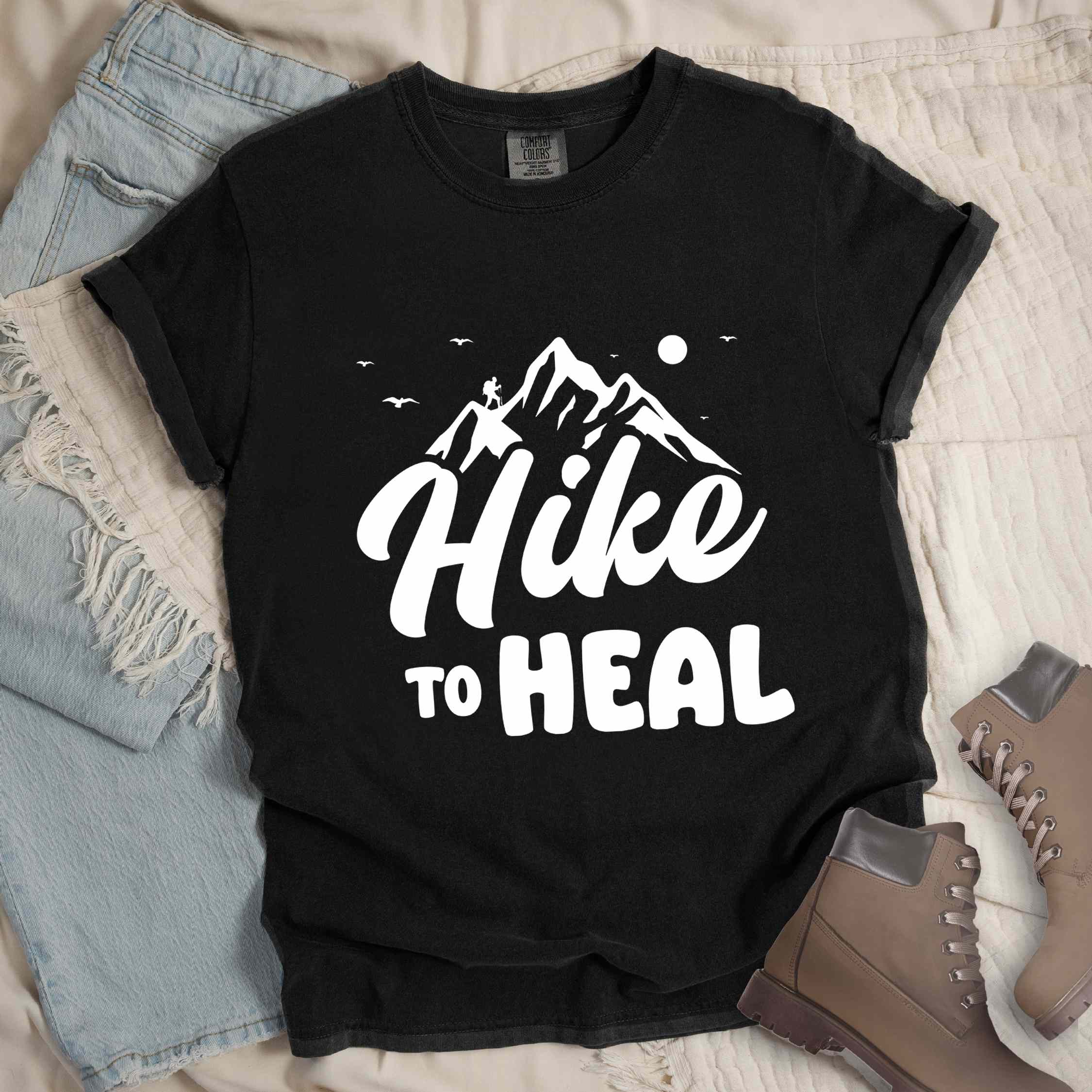 Black "Hike to Heal" colored statement tee with bold typography, mountain, sunrise, perfect for adventure driven individuals.