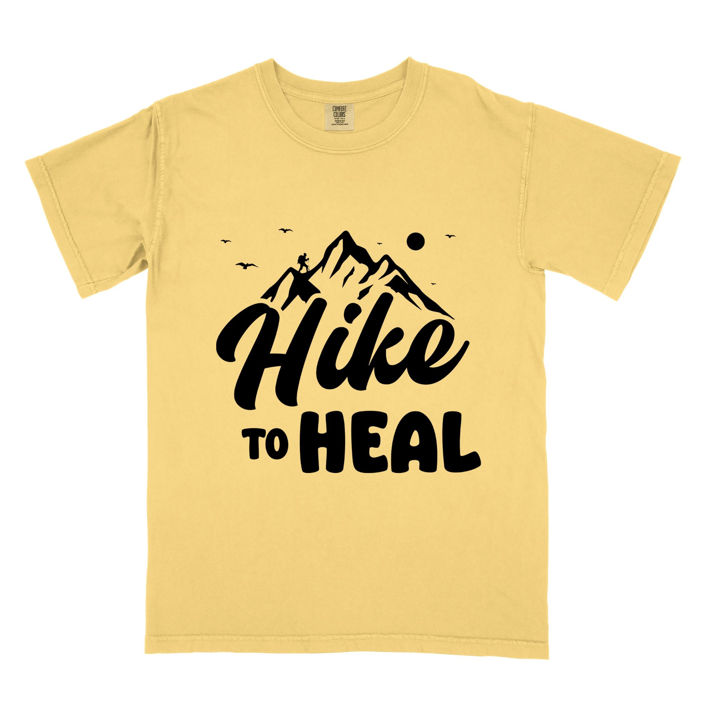 Butter "Hike to Heal" colored statement tee with bold typography, mountain, sunrise, perfect for adventure driven individuals.