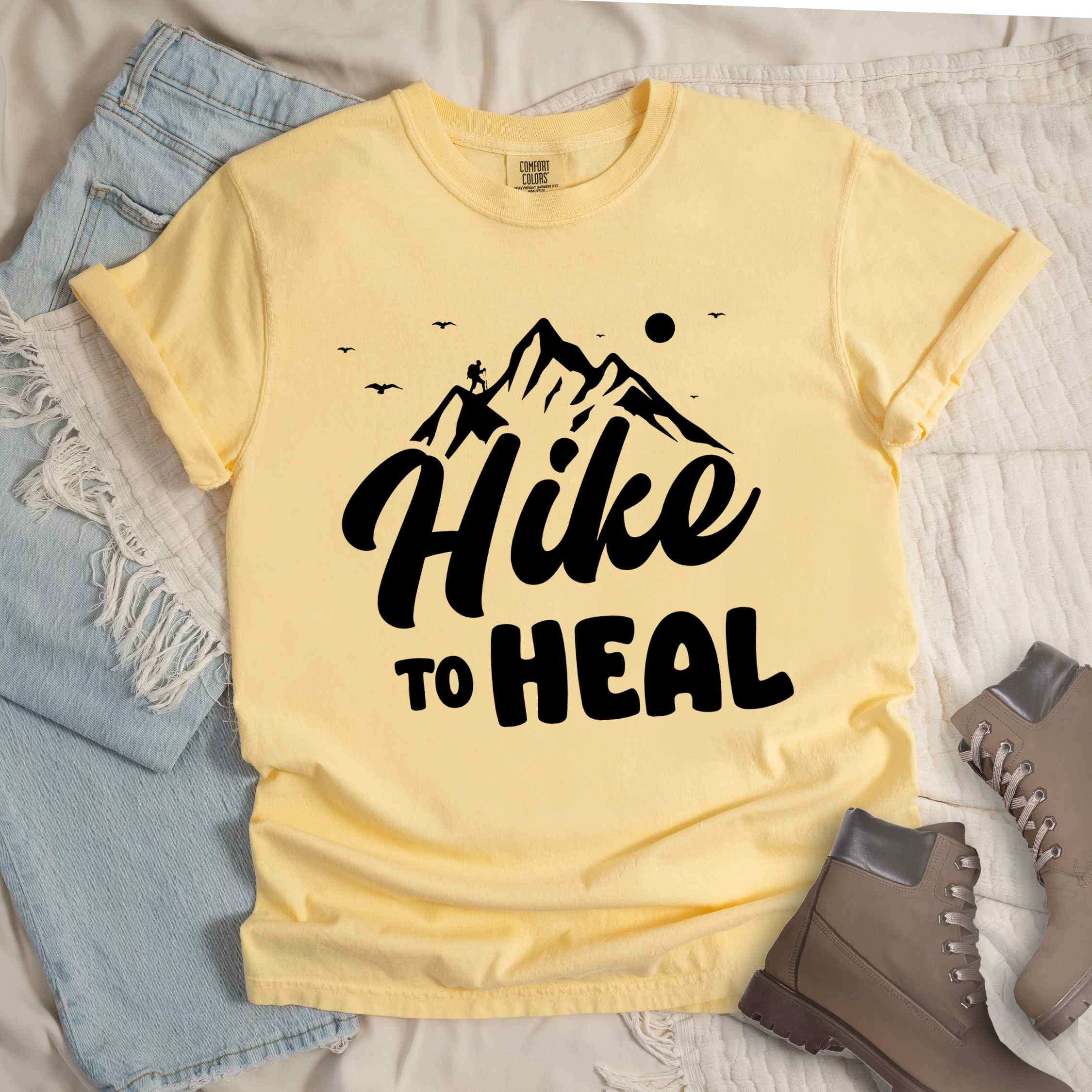 Butter "Hike to Heal" colored statement tee with bold typography, mountain, sunrise, perfect for adventure driven individuals.