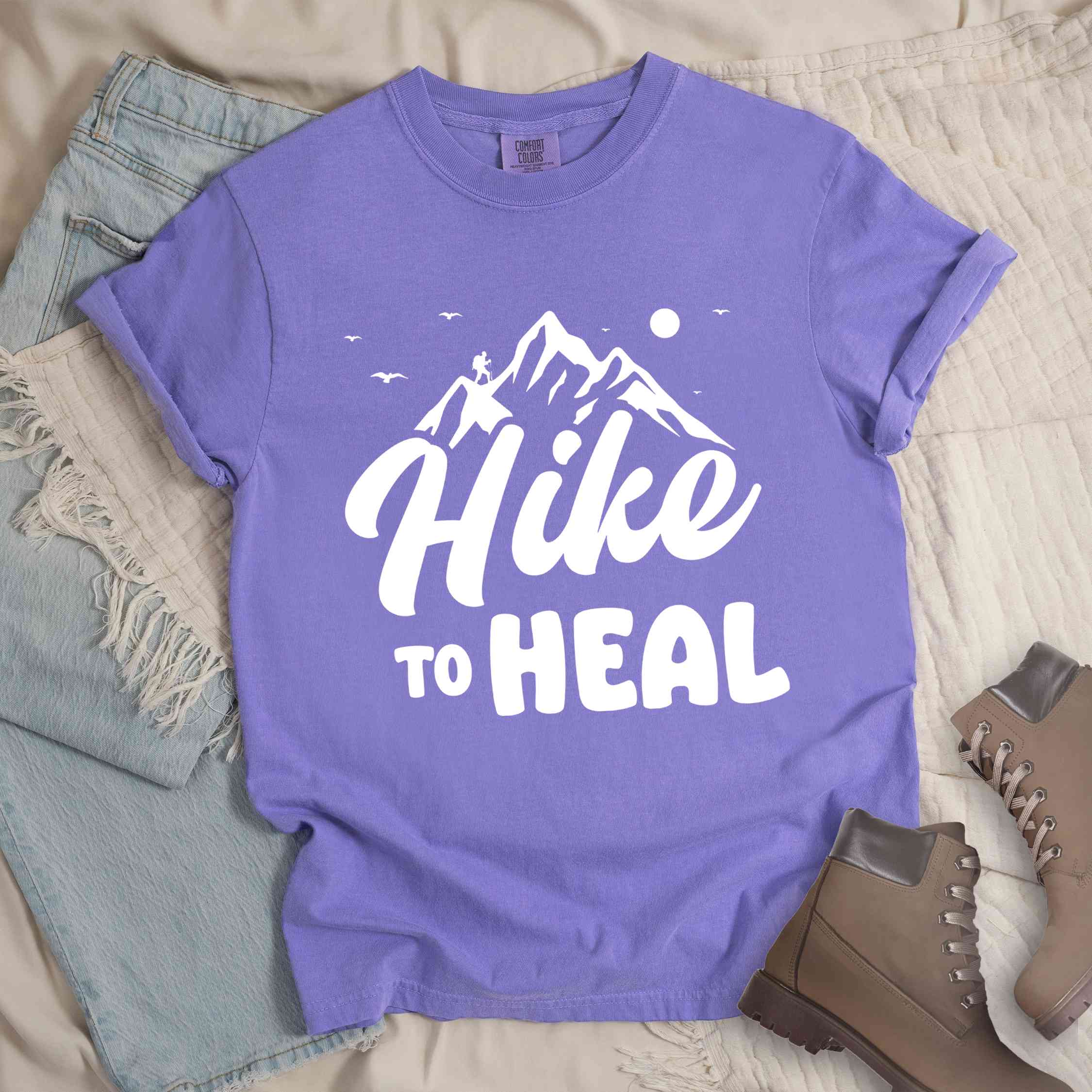 Violet "Hike to Heal" colored statement tee with bold typography, mountain, sunrise, perfect for adventure driven individuals.