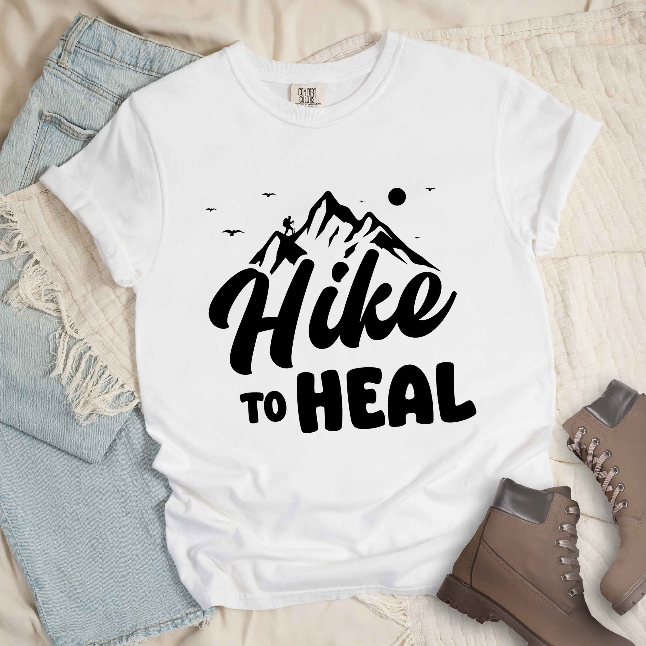 White "Hike to Heal" colored statement tee with bold typography, mountain, sunrise, perfect for adventure driven individuals.