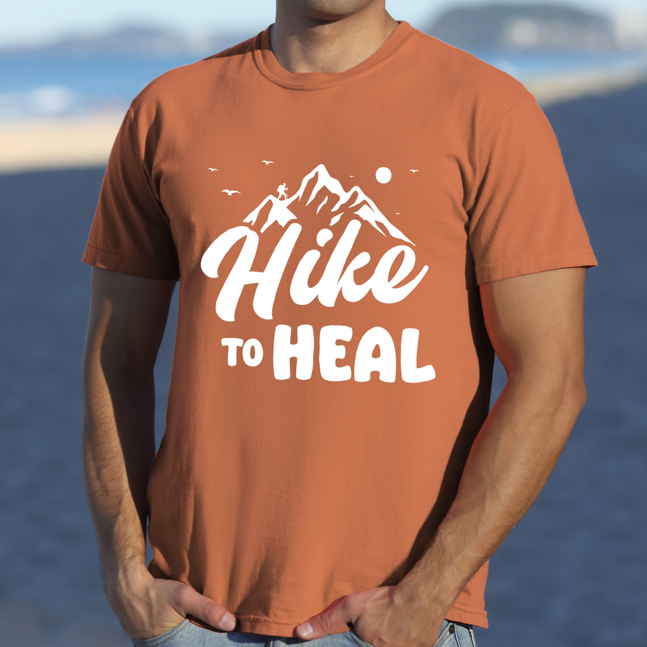 Man wearing yam "Hike to Heal" colored statement tee with bold typography, mountain, sunrise, perfect for adventure driven individuals.