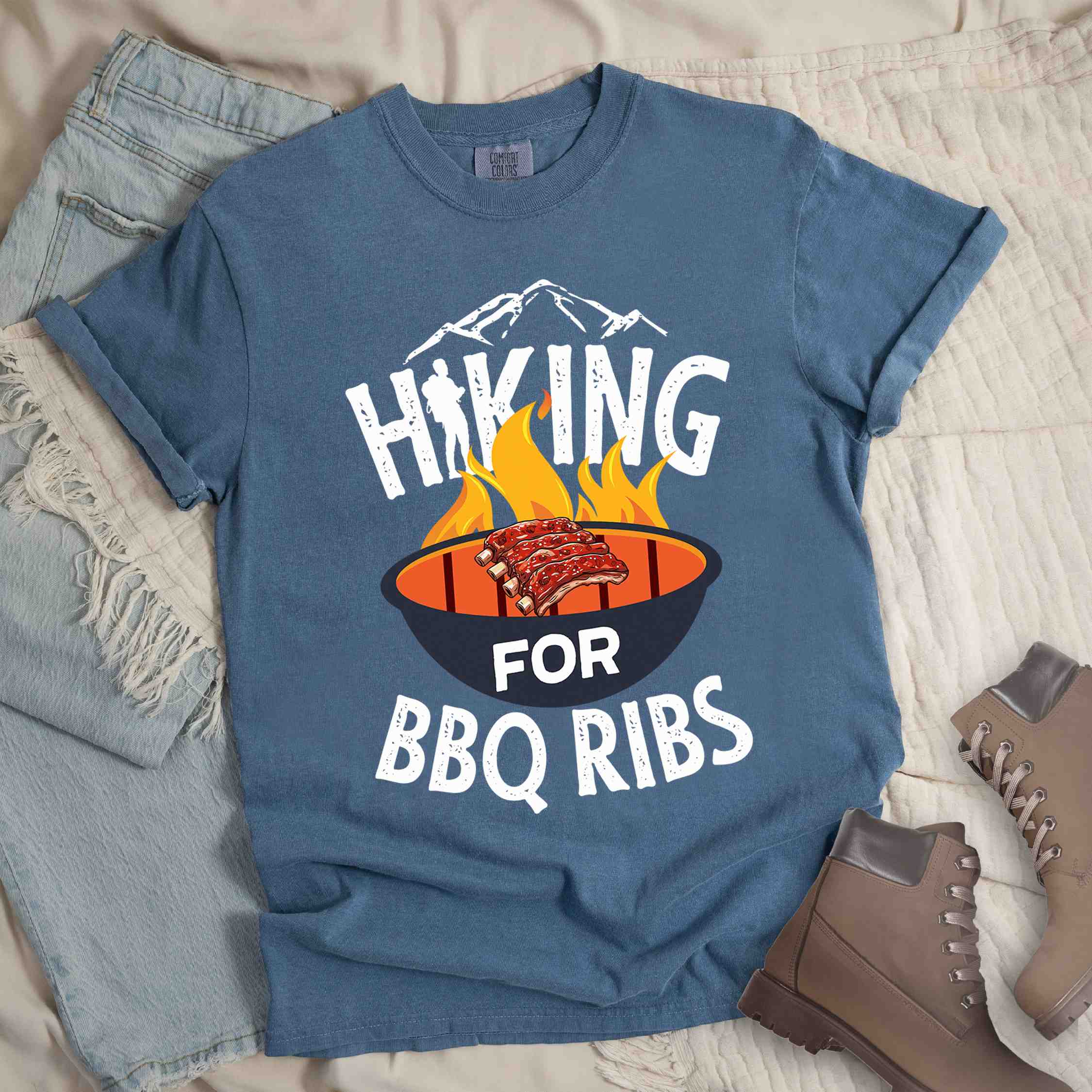 Blue jean Hiking for BBQ ribs colored vintage tee with bold typography, illustrated grilling bbq ribs, mountains, birds, and bbq enthusiasts