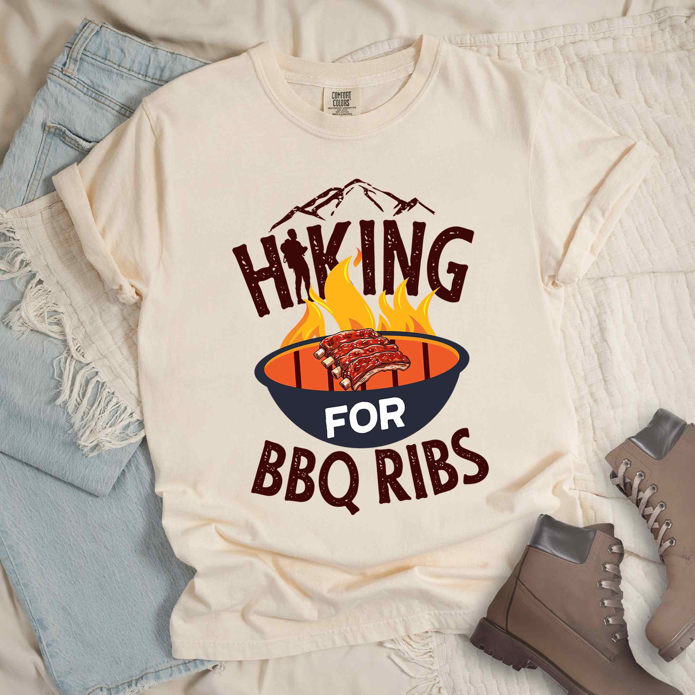 Ivory Hiking for BBQ ribs colored vintage tee with bold typography, illustrated grilling bbq ribs, mountains, birds, and bbq enthusiasts