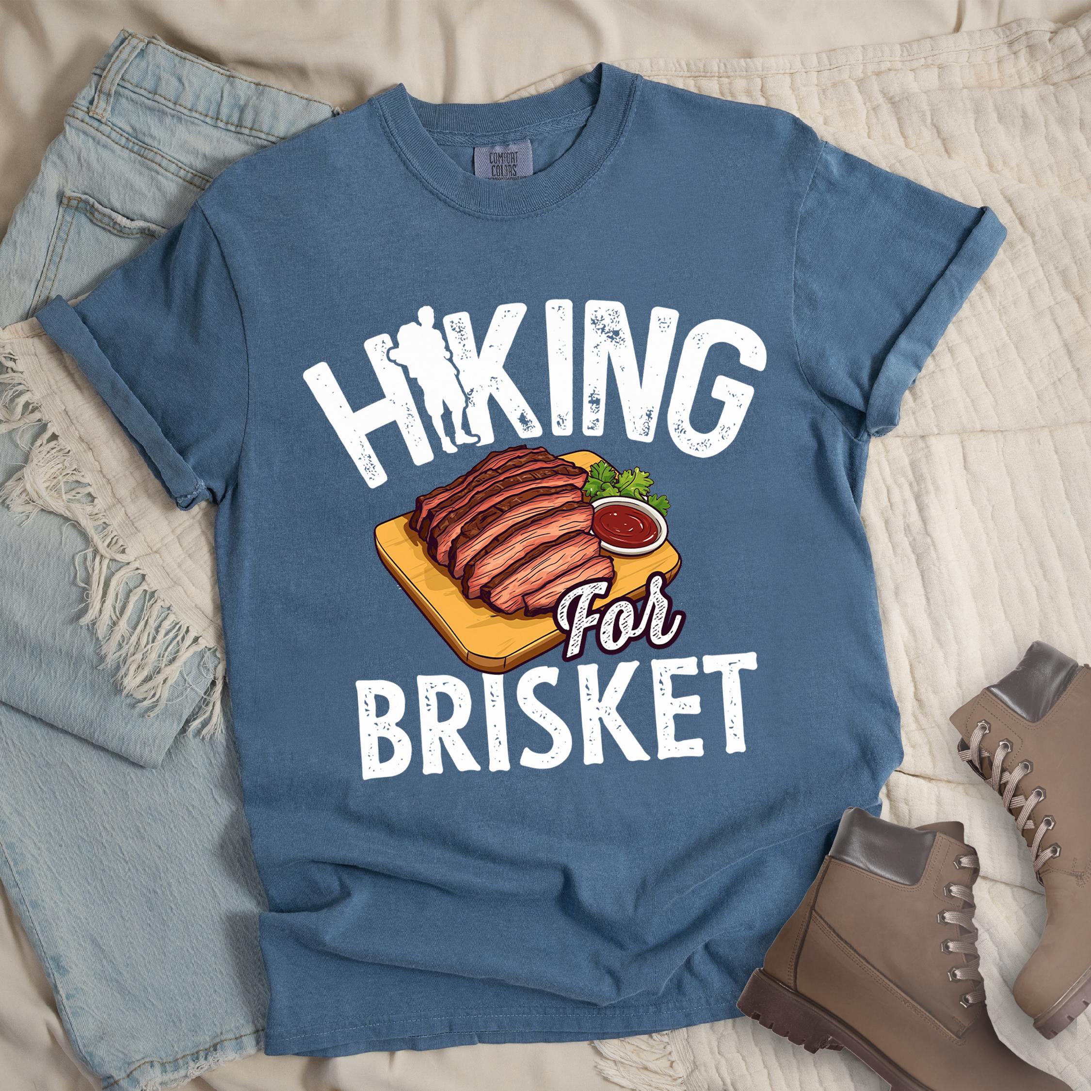 Dark blue shirt with “Hiking for Brisket” text, featuring a hiker silhouette, mountain outline, and a cutting board topped with sliced brisket and barbecue sauce.