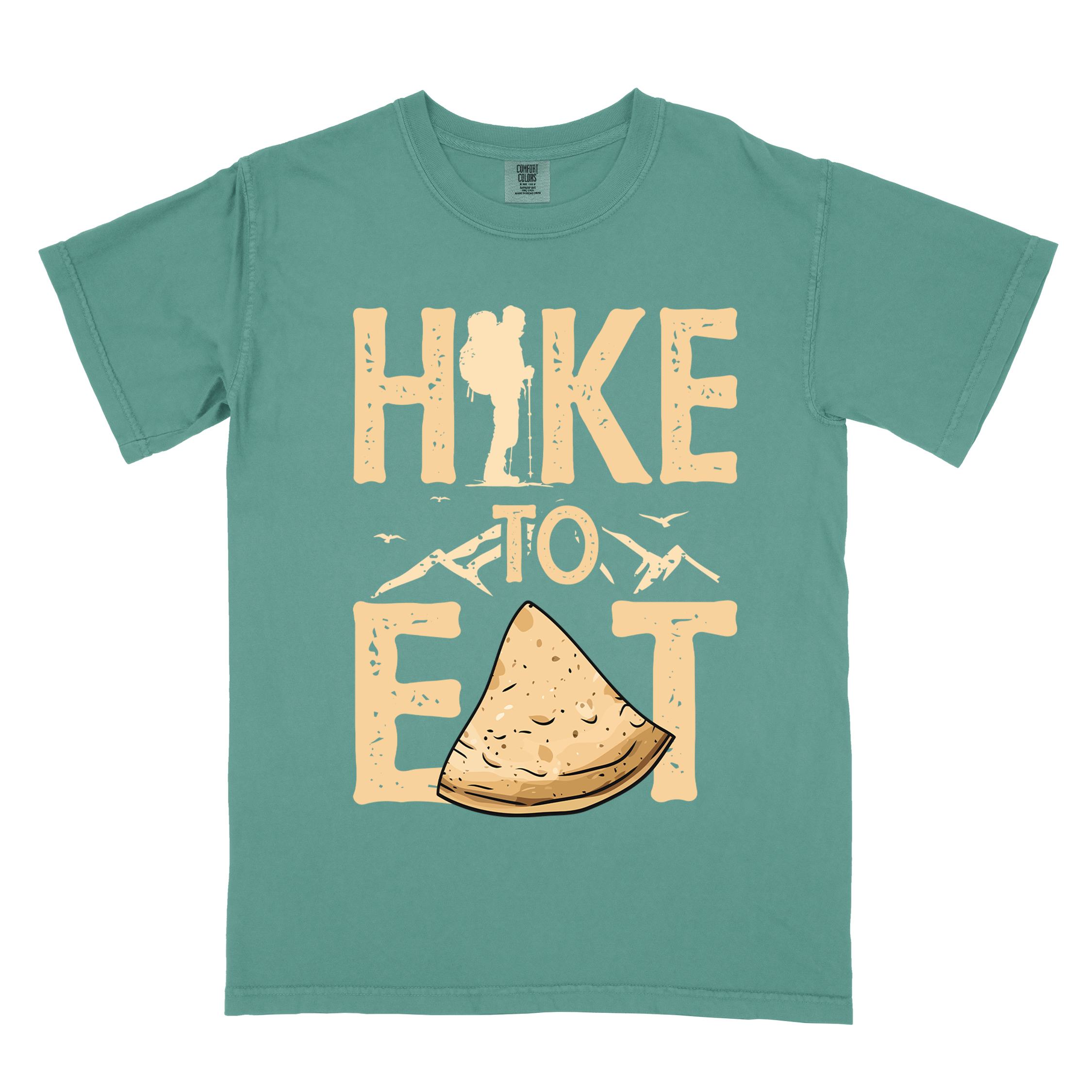 Light green "Hike to Eat" colored statement tee with bold typography, mountain, illustrated tortilla, perfect for tortilla lovers.